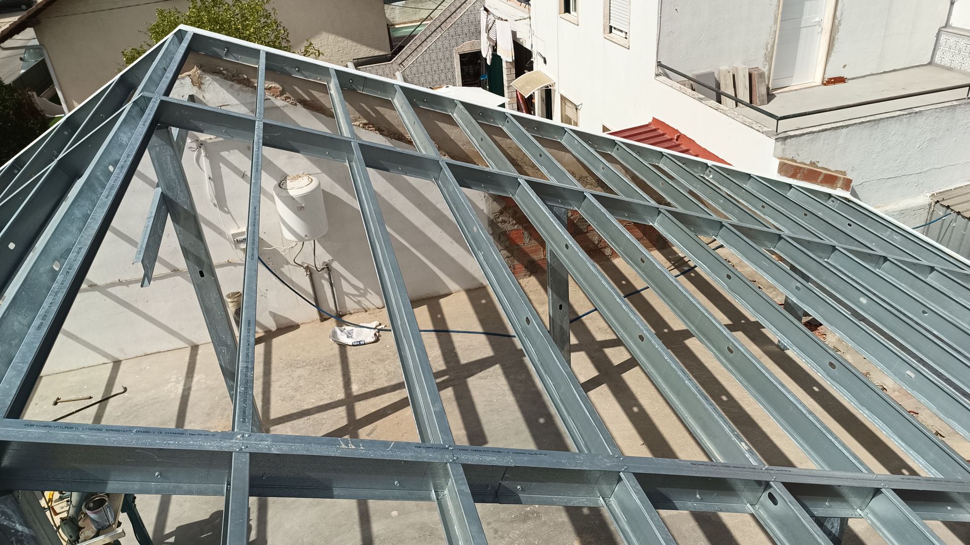 Telhado com estrutura de aço em construção em um edifício, com a cidade ao fundo.