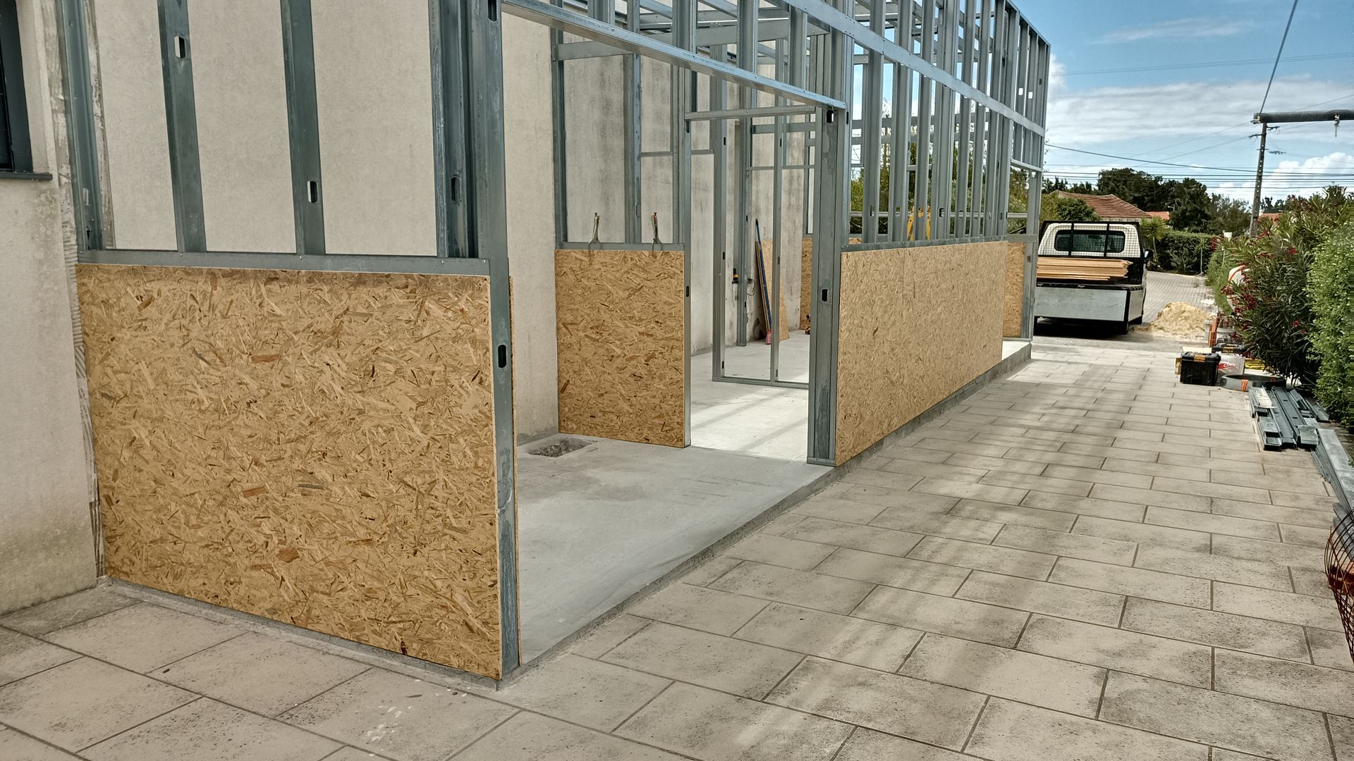 Canteiro de obras: Estrutura metálica com revestimento em OSB. Entrada de veículos na frente.