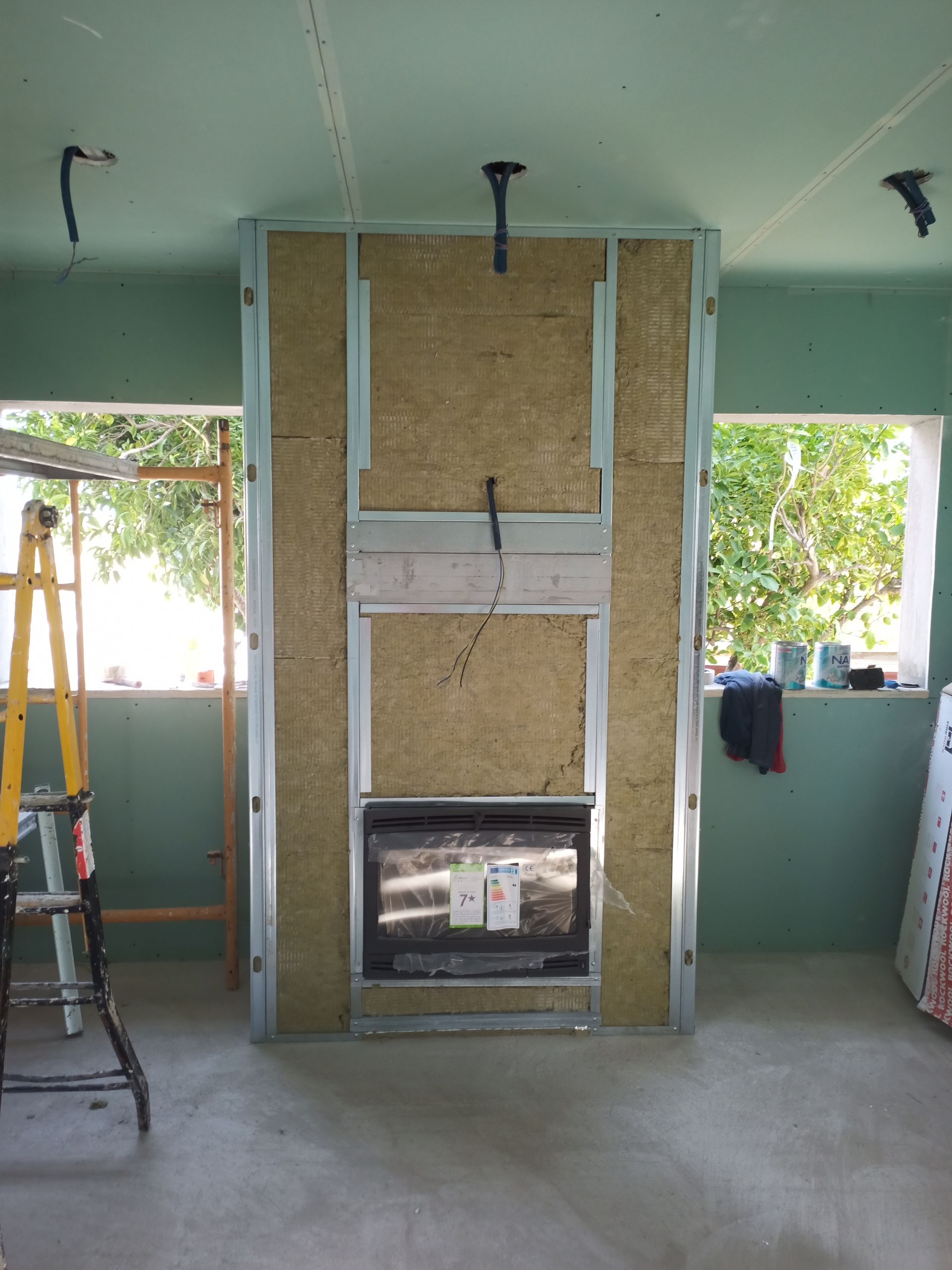 Lareira em construção, estrutura metálica com isolamento e inserto elétrico instalado. Paredes verdes, cômodo inacabado.