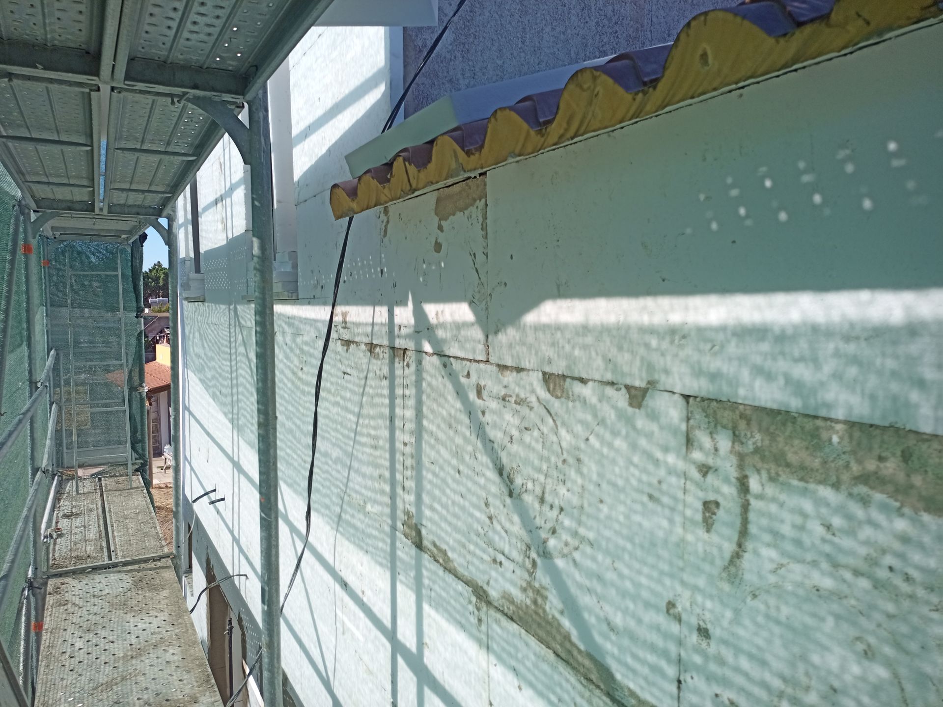 Exterior do edifício com andaimes, isolamento e estuque parcialmente acabado.