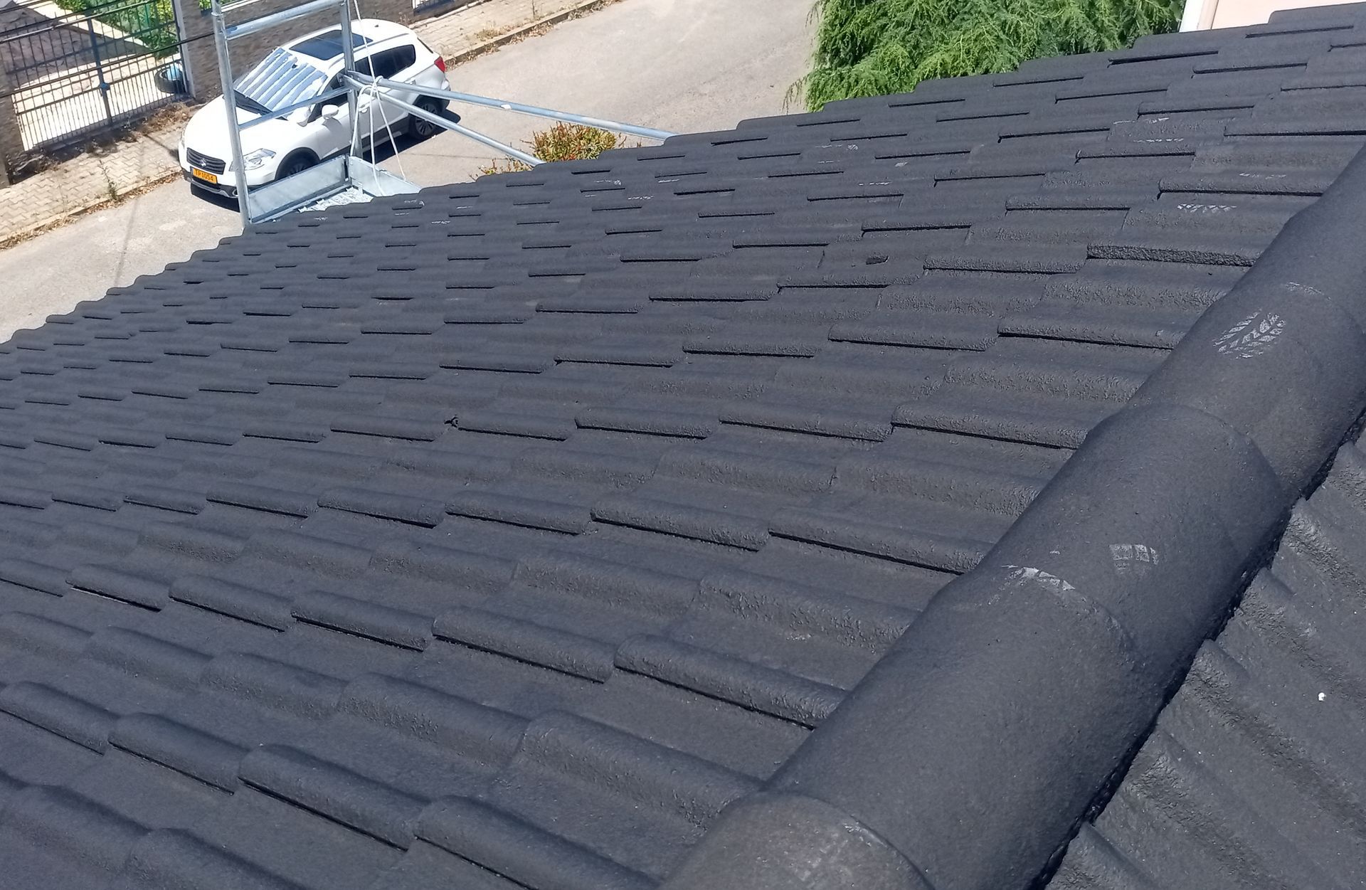 Telhado de telhas cinza-escuras com borda curva, em um ambiente externo com um carro branco visível.