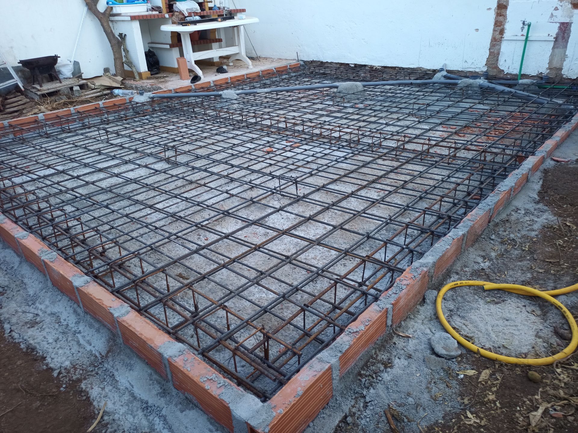 Fundação de concreto armado em construção; borda de tijolos, grade de vergalhões de metal, ambiente externo.