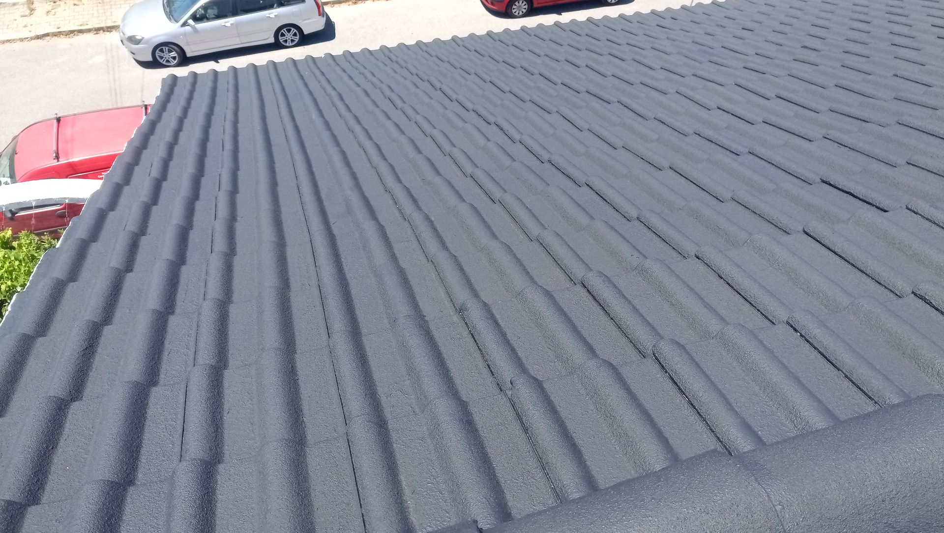 Telhado de metal ondulado cinza em um prédio, vista em ângulo. Carros e rua visíveis ao fundo.