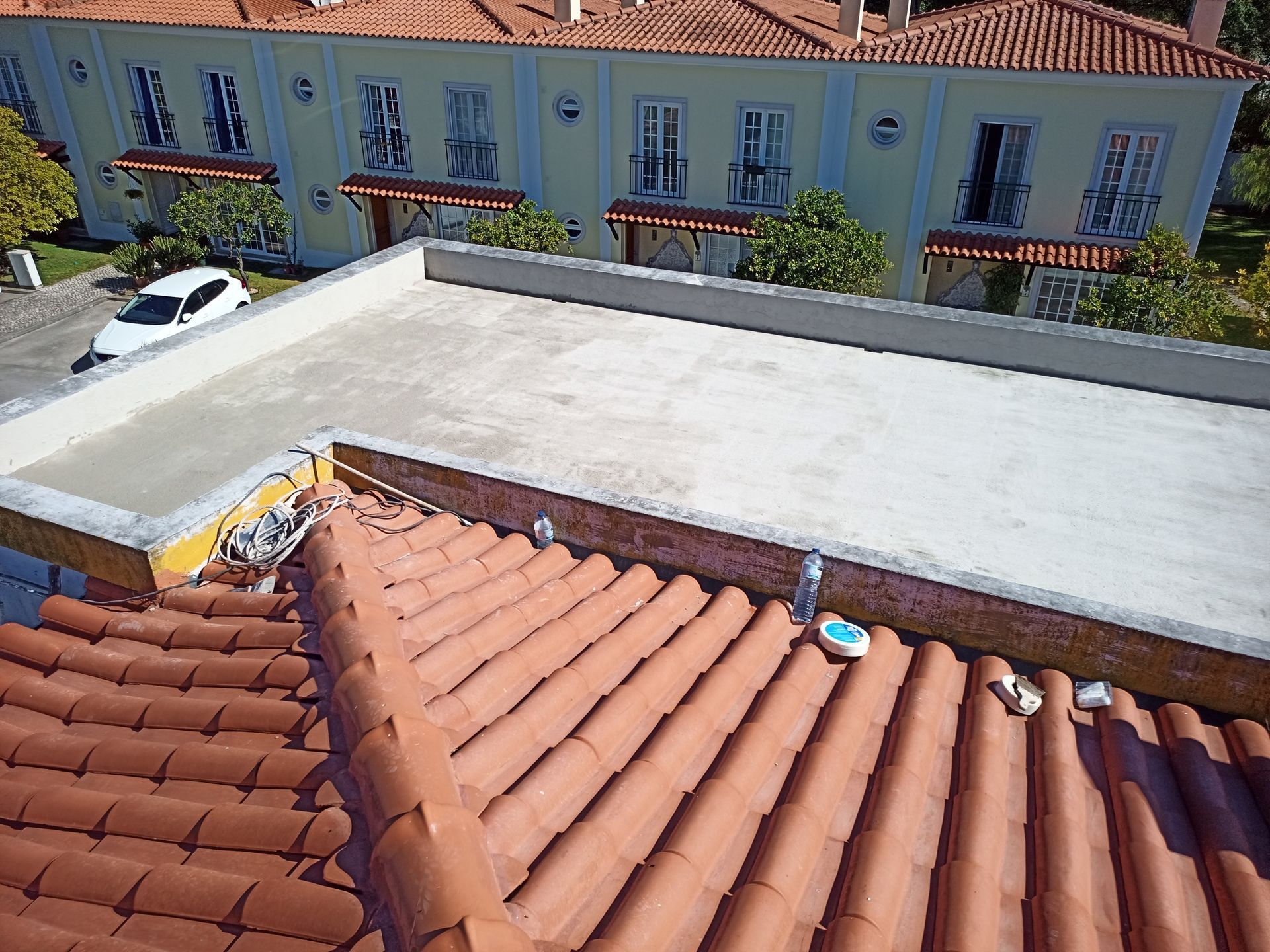 Vista de um telhado plano e claro ao lado de um telhado de telhas vermelhas, com um edifício ao fundo.