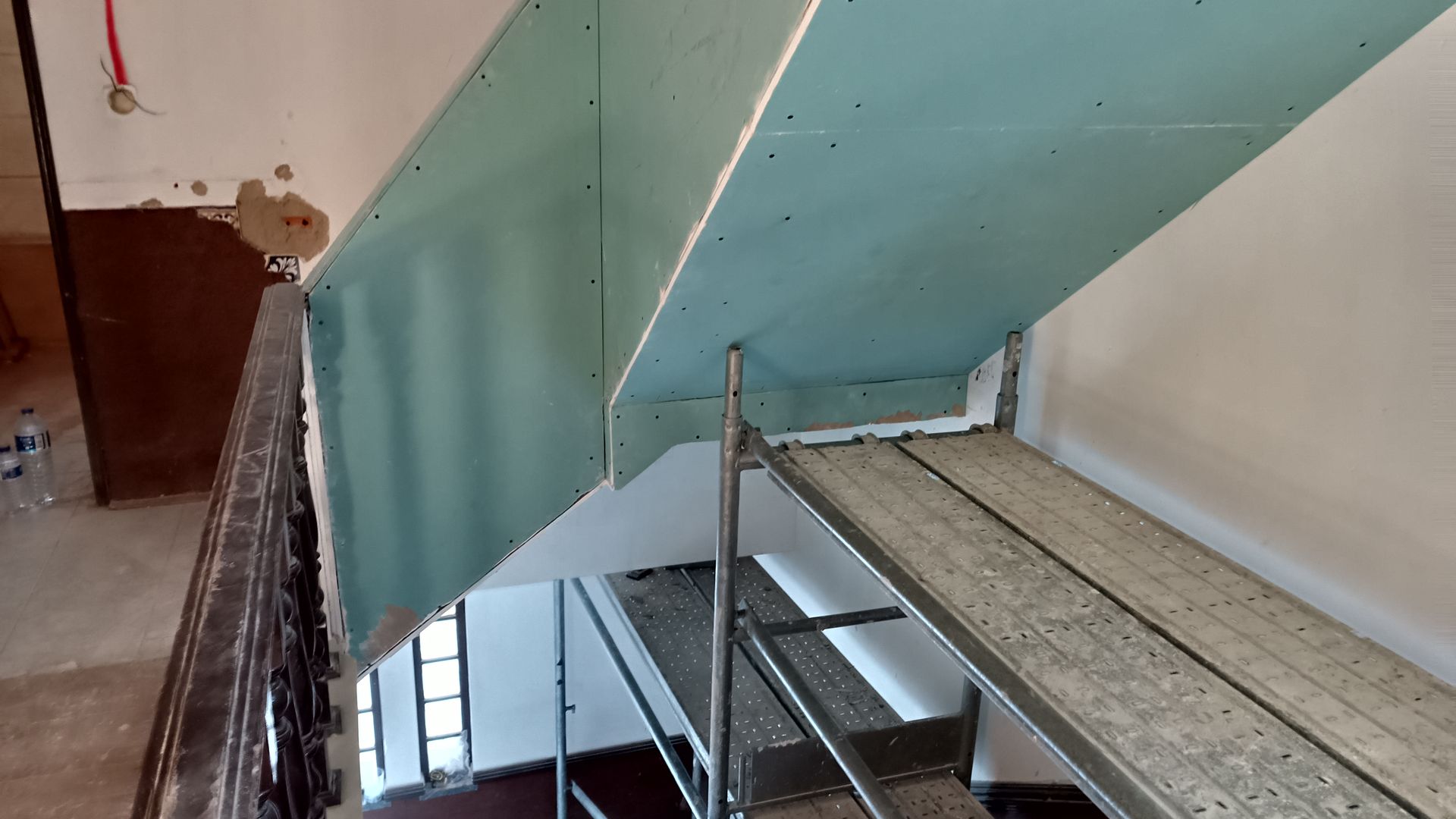 Instalação de drywall em escadaria. O andaime, de cor azul-esverdeada, dá suporte ao drywall.