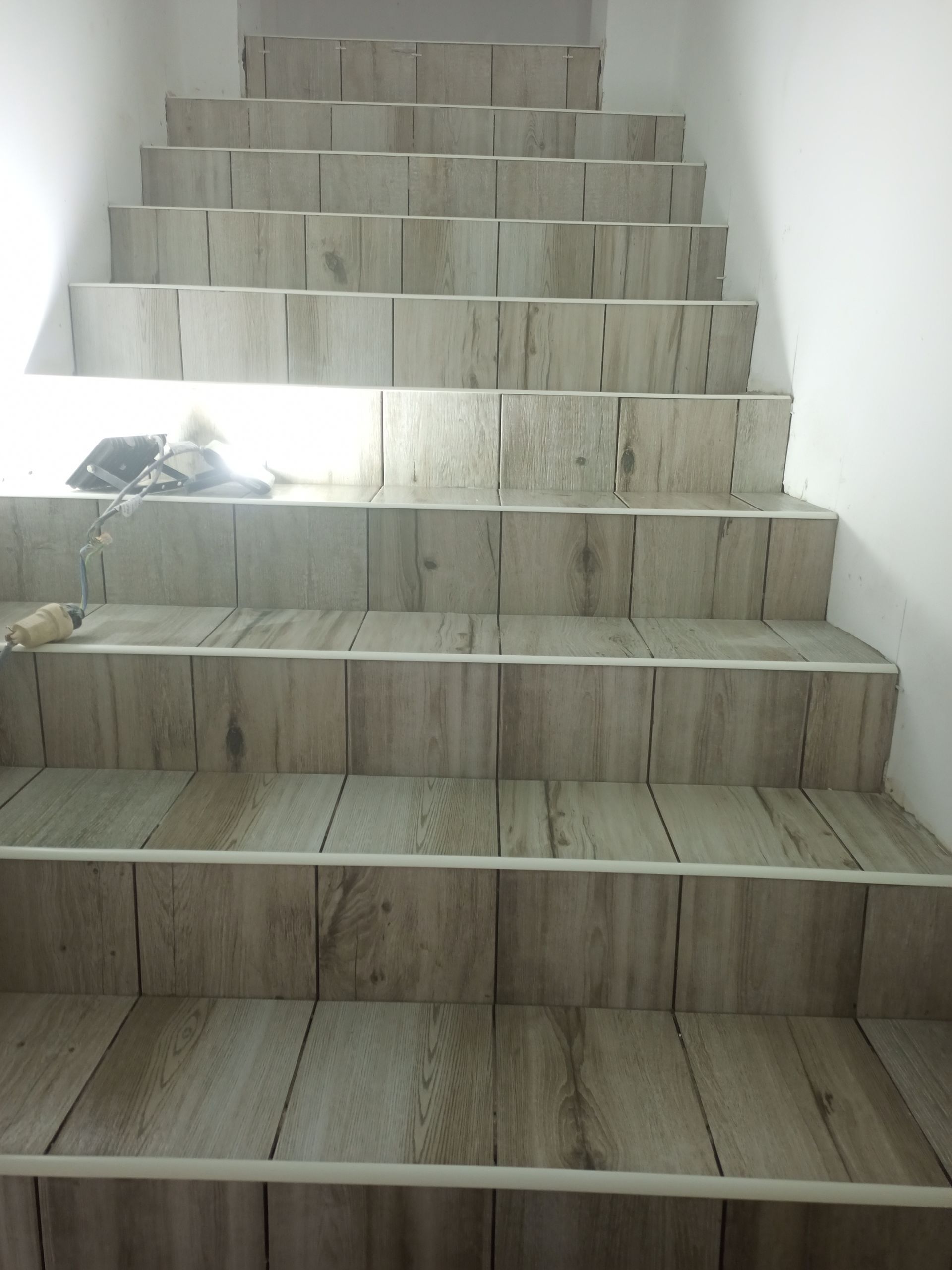 Escada com piso de madeira que leva ao andar superior. Paredes brancas em ambos os lados.