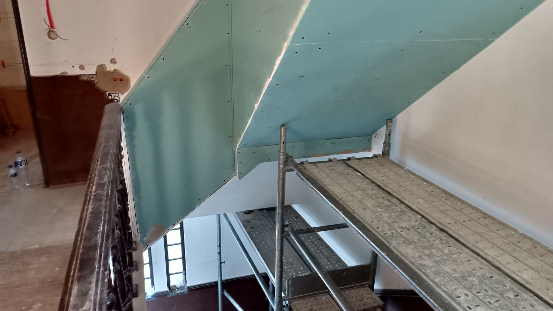 Placas de gesso instaladas no teto da escada; andaimes embaixo.