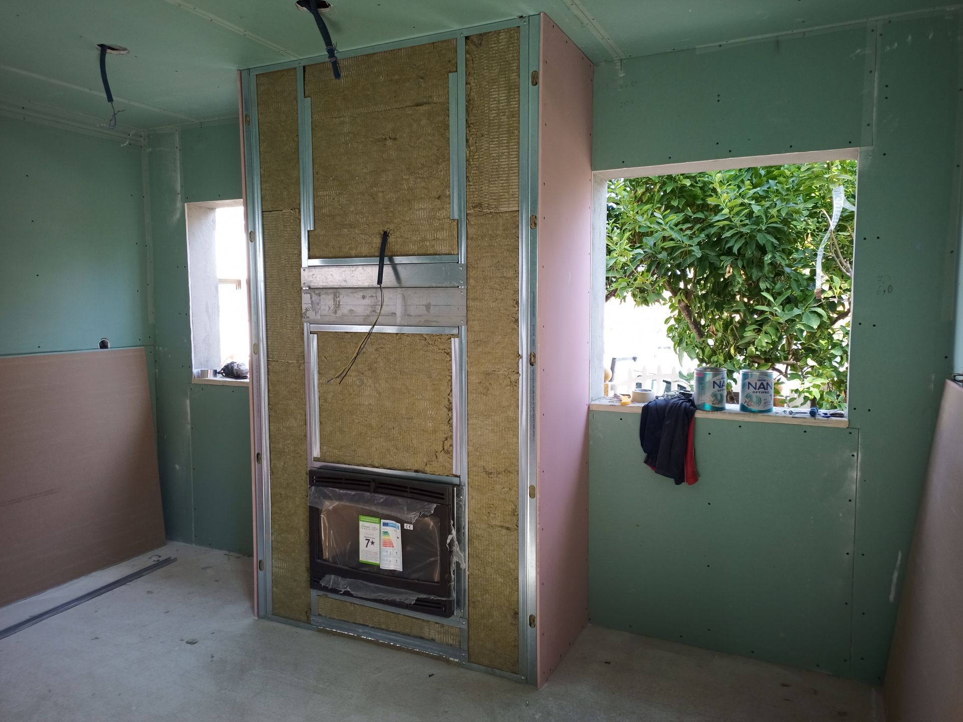 Interior em construção com lareira emoldurada em perfis metálicos e isolada.