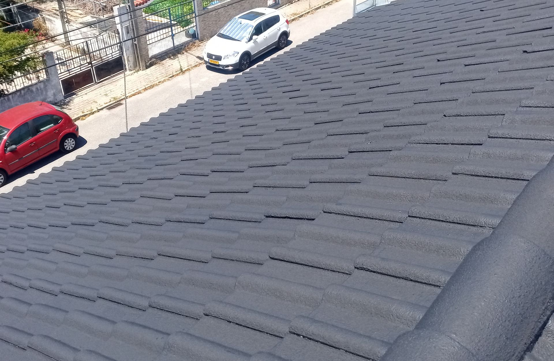 Telhas cinza-escuras com uma rua e carros ao fundo.