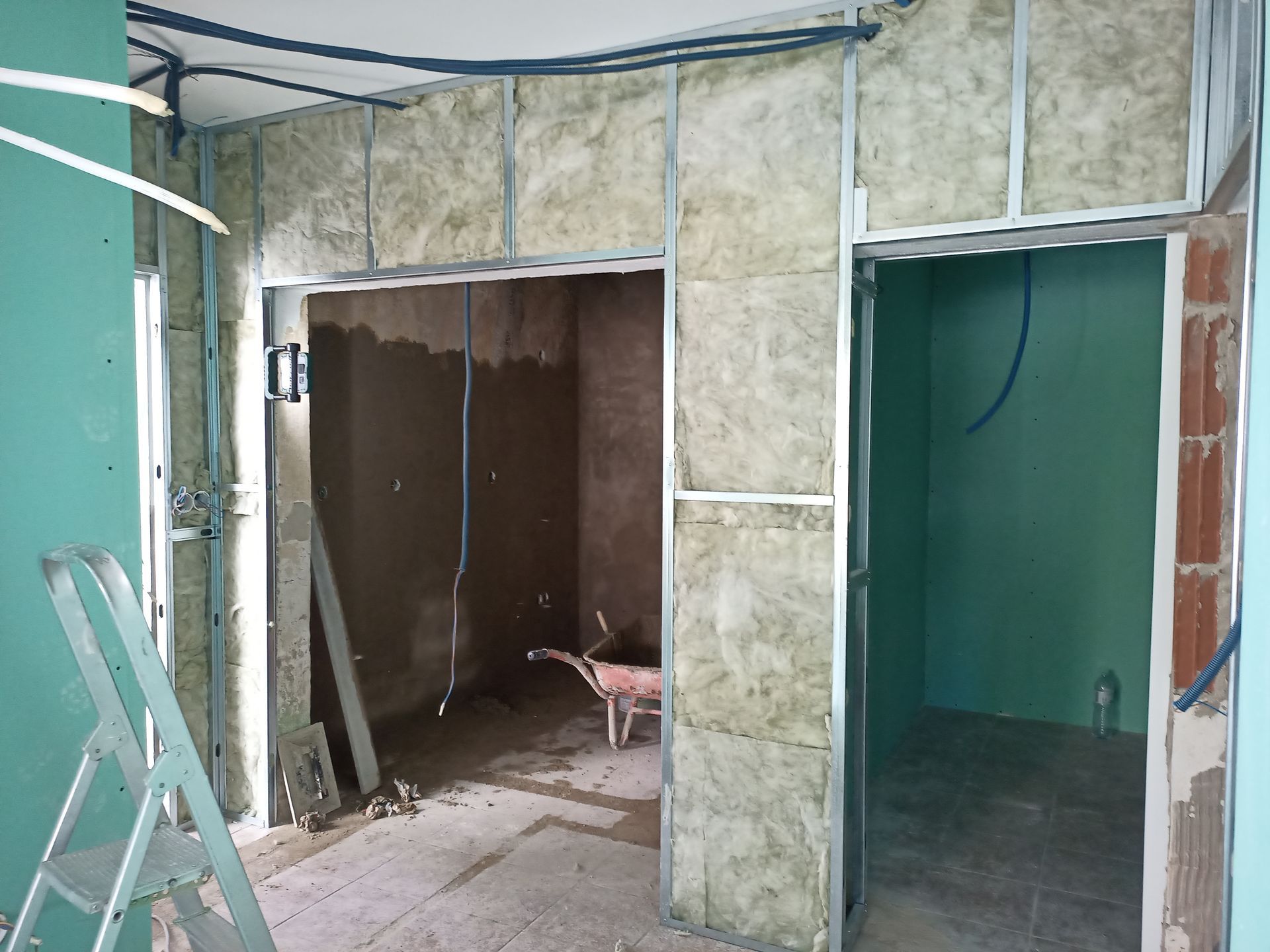Vista interna de uma sala em construção com estrutura metálica, isolamento e portas.