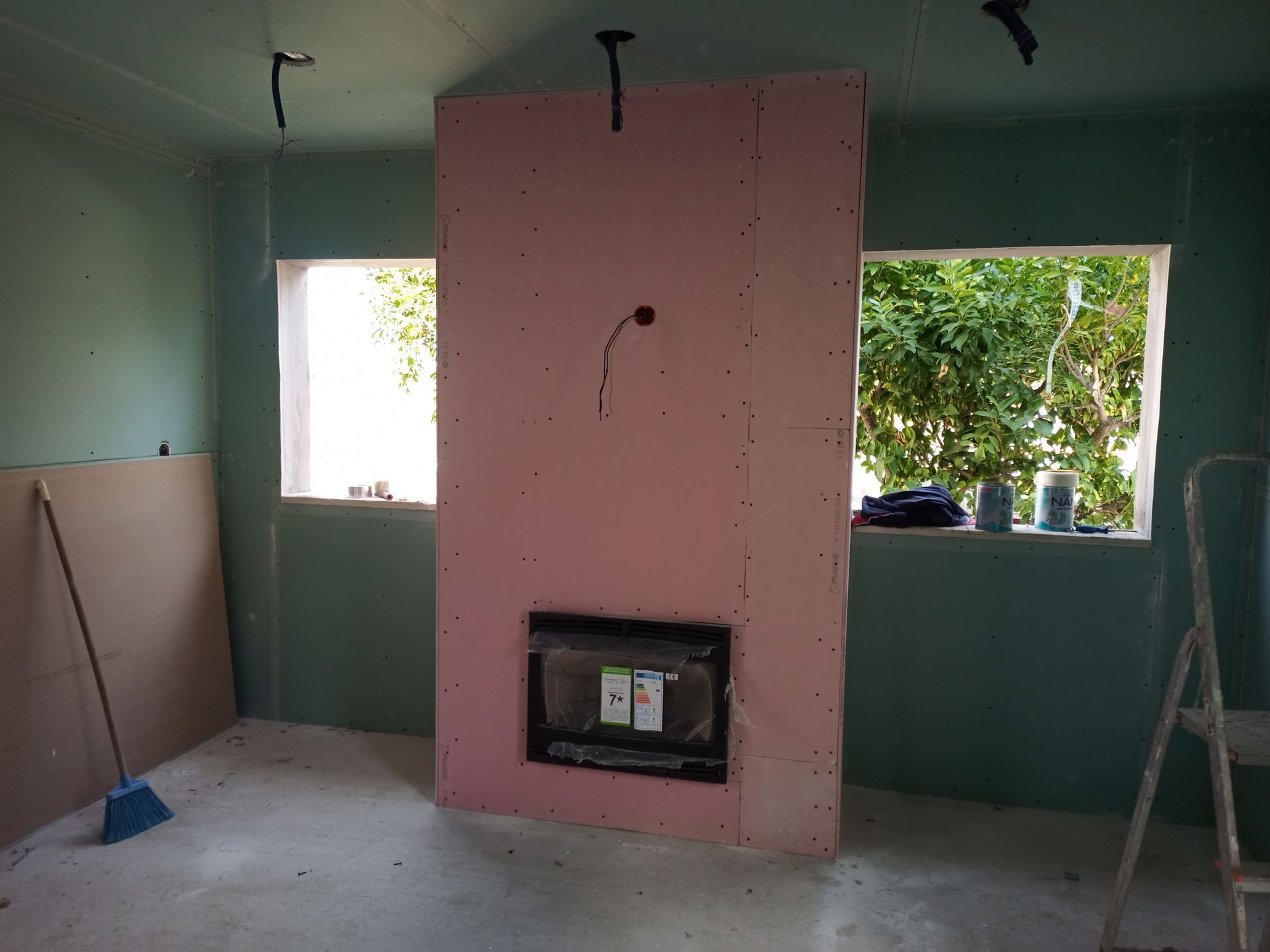 Quarto em construção com lareira isolada rosa, janelas e paredes verdes.