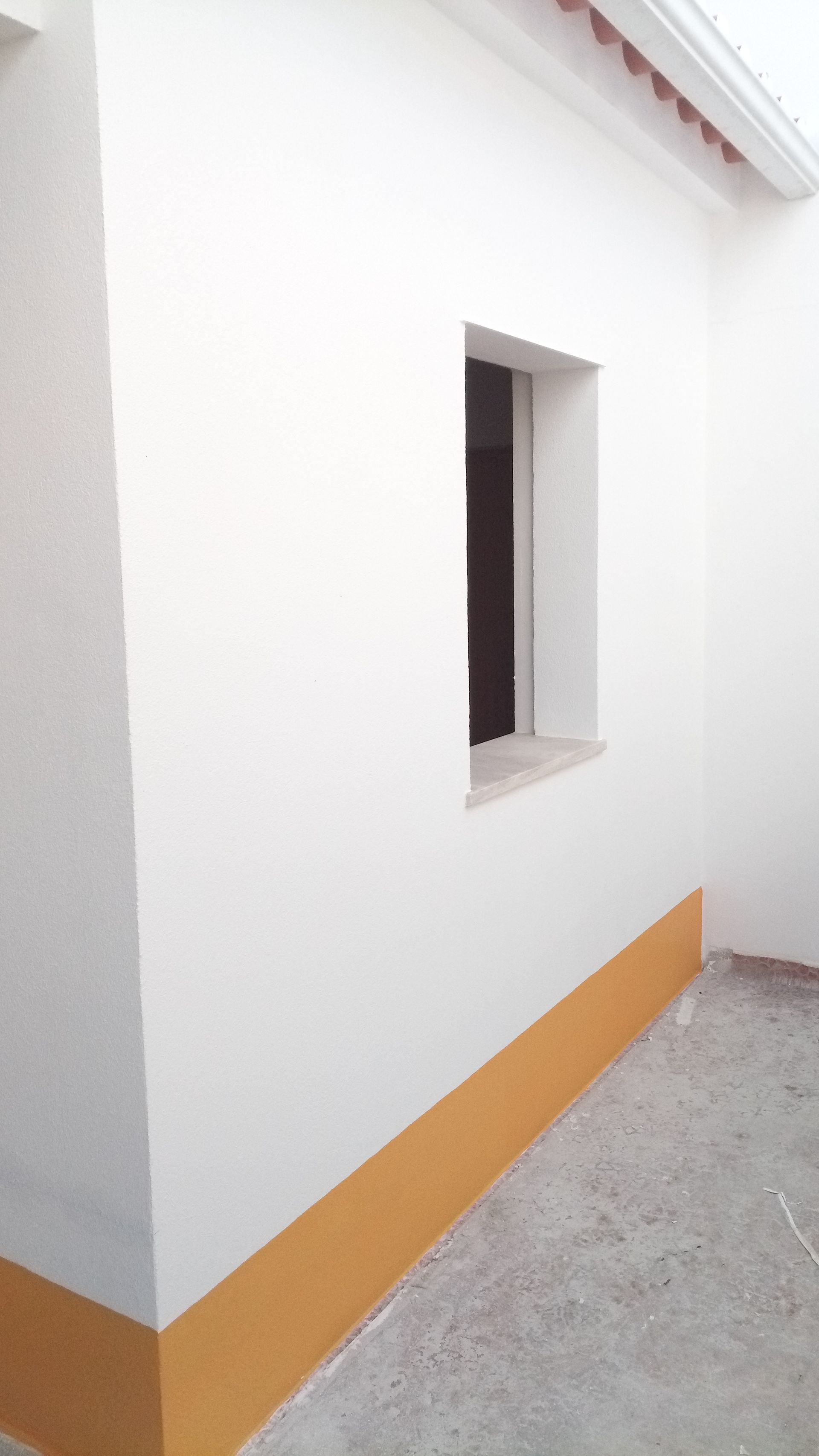 Exterior branco do prédio com uma pequena janela e base pintada de amarelo.
