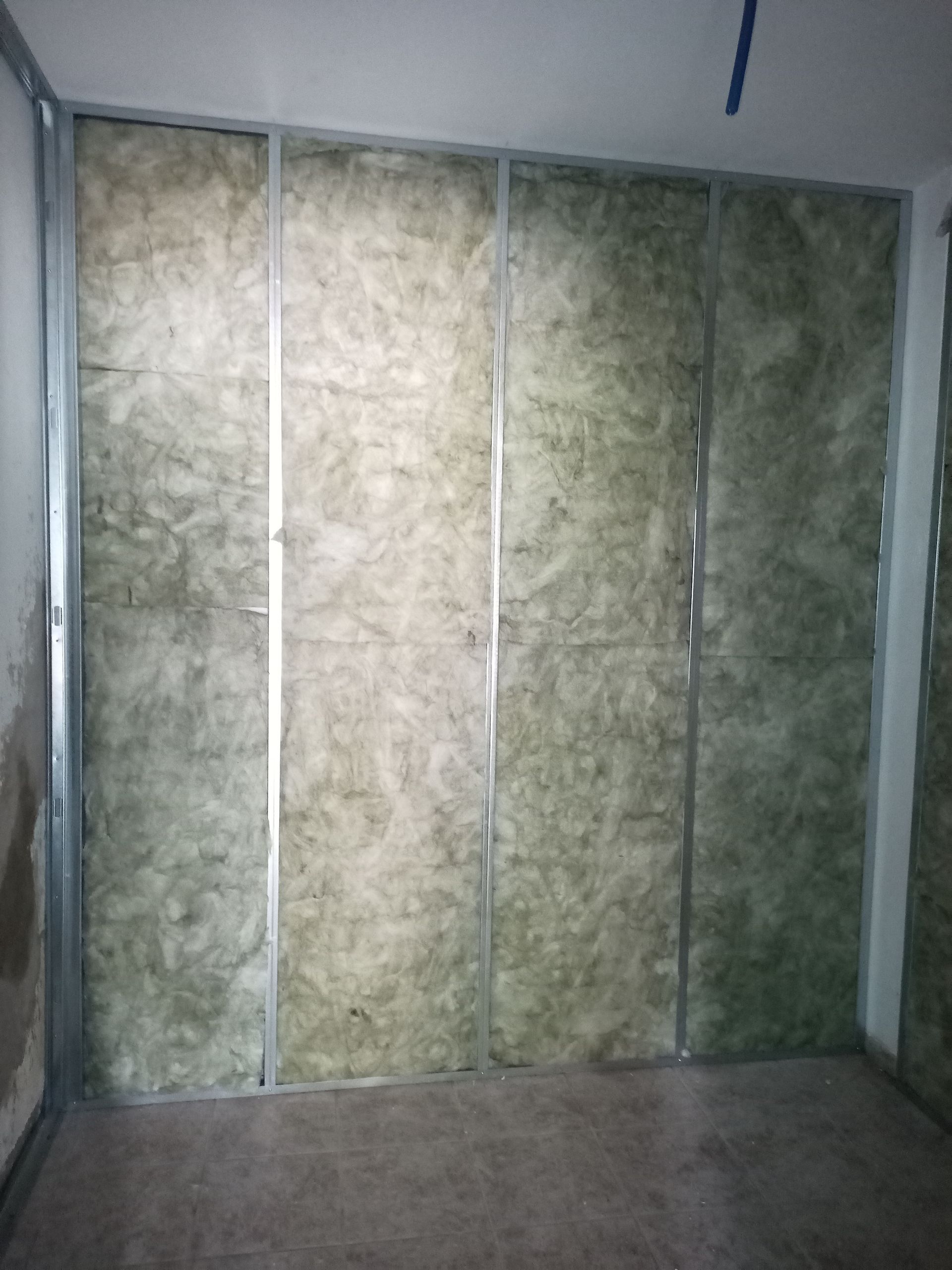 Parede interna em construção; estrutura metálica com isolamento entre os montantes; cômodo inacabado.