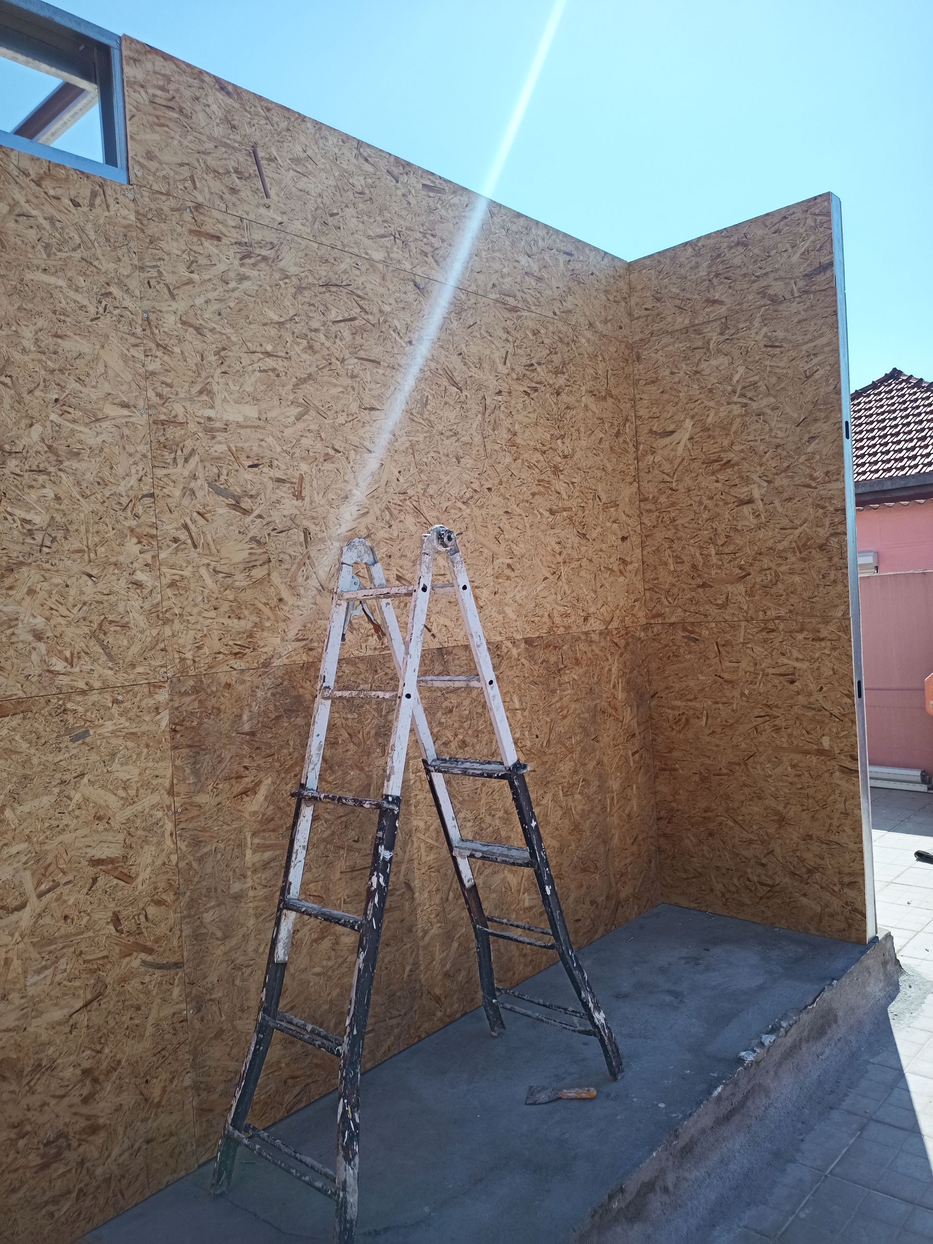 Construção: Paredes de aglomerado de madeira, escada encostada na parede, vista externa.