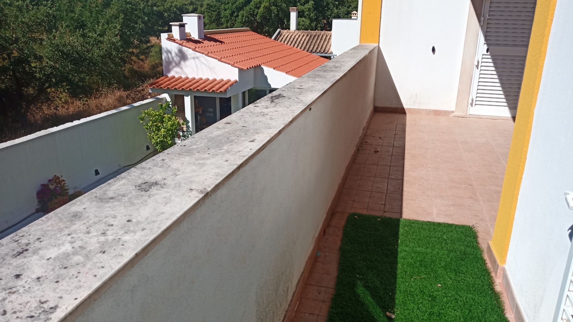 Varanda com guarda-corpo de concreto, vista para prédios residenciais e área verde.