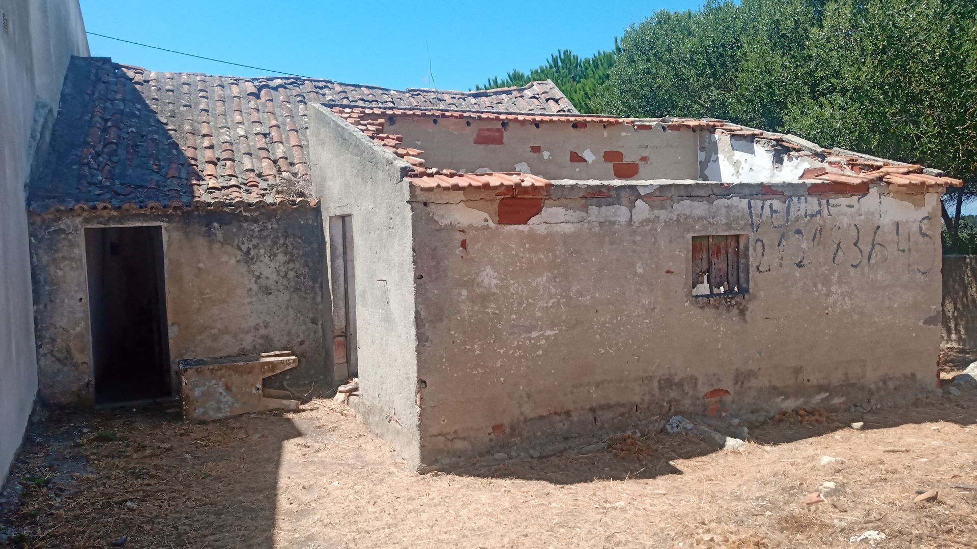 Prédio dilapidado com telhas faltando, paredes desgastadas e porta aberta, situado ao ar livre.