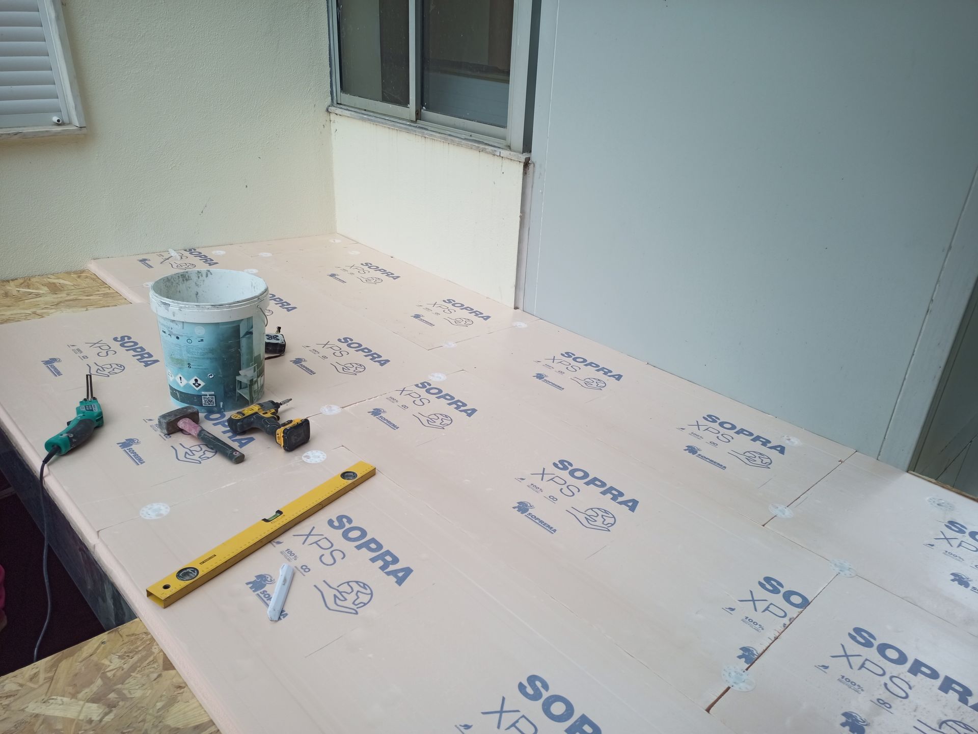 Canteiro de obras: placas de isolamento de espuma rosa no piso de uma varanda, ferramentas e balde presentes.