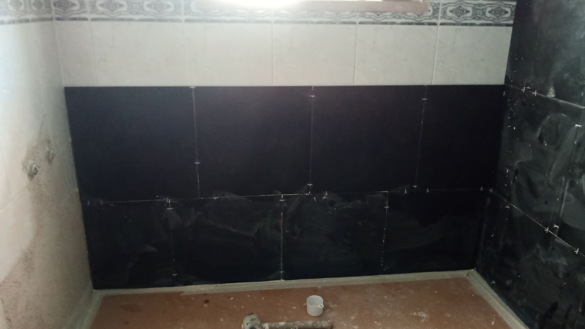 Paredes do banheiro com azulejos pretos, azulejos brancos e faixa decorativa; construção inacabada.