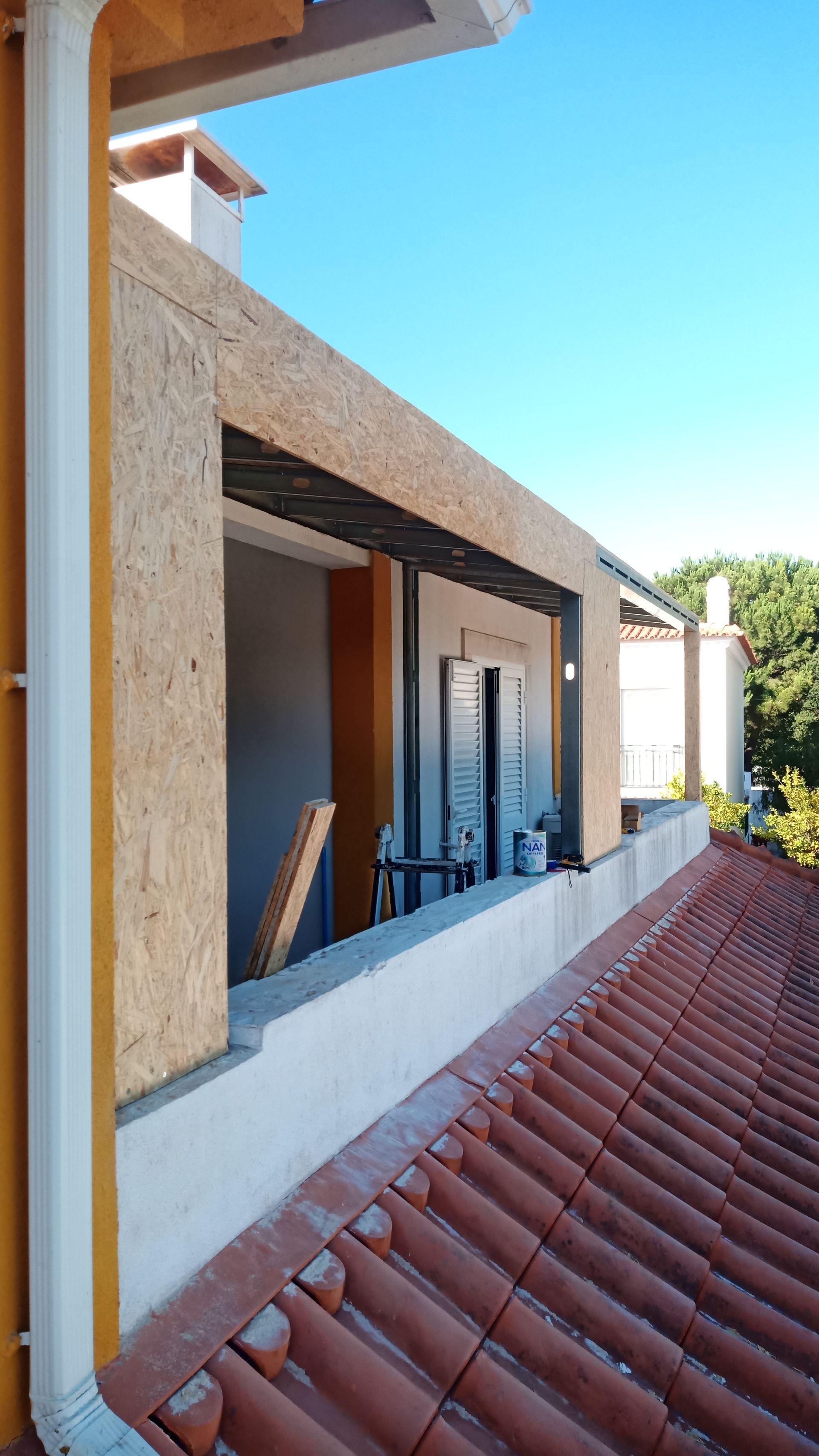 Exterior do edifício com estrutura de madeira aparente e varanda, telhado de telha vermelha e céu azul.