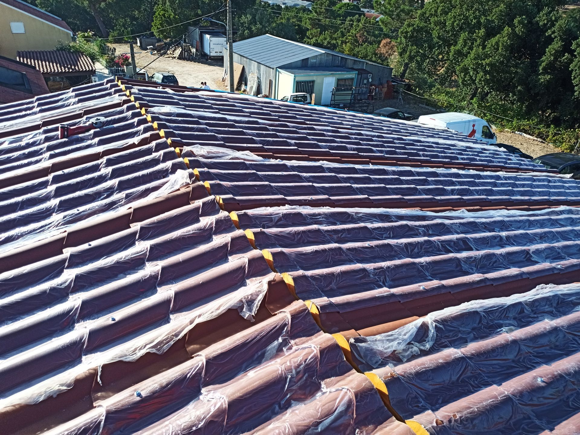 Telhado de telha vermelha parcialmente coberto com lona plástica em um dia ensolarado.