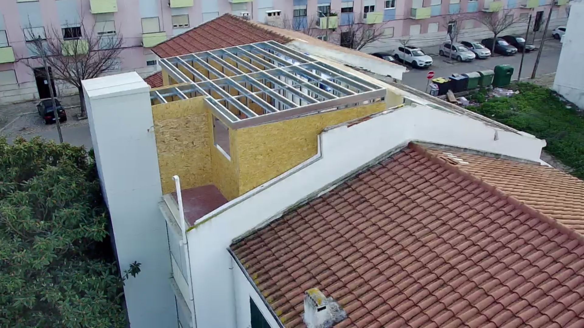 Telhado de um edifício em construção; estrutura metálica, painéis de madeira e telha vermelha visíveis.