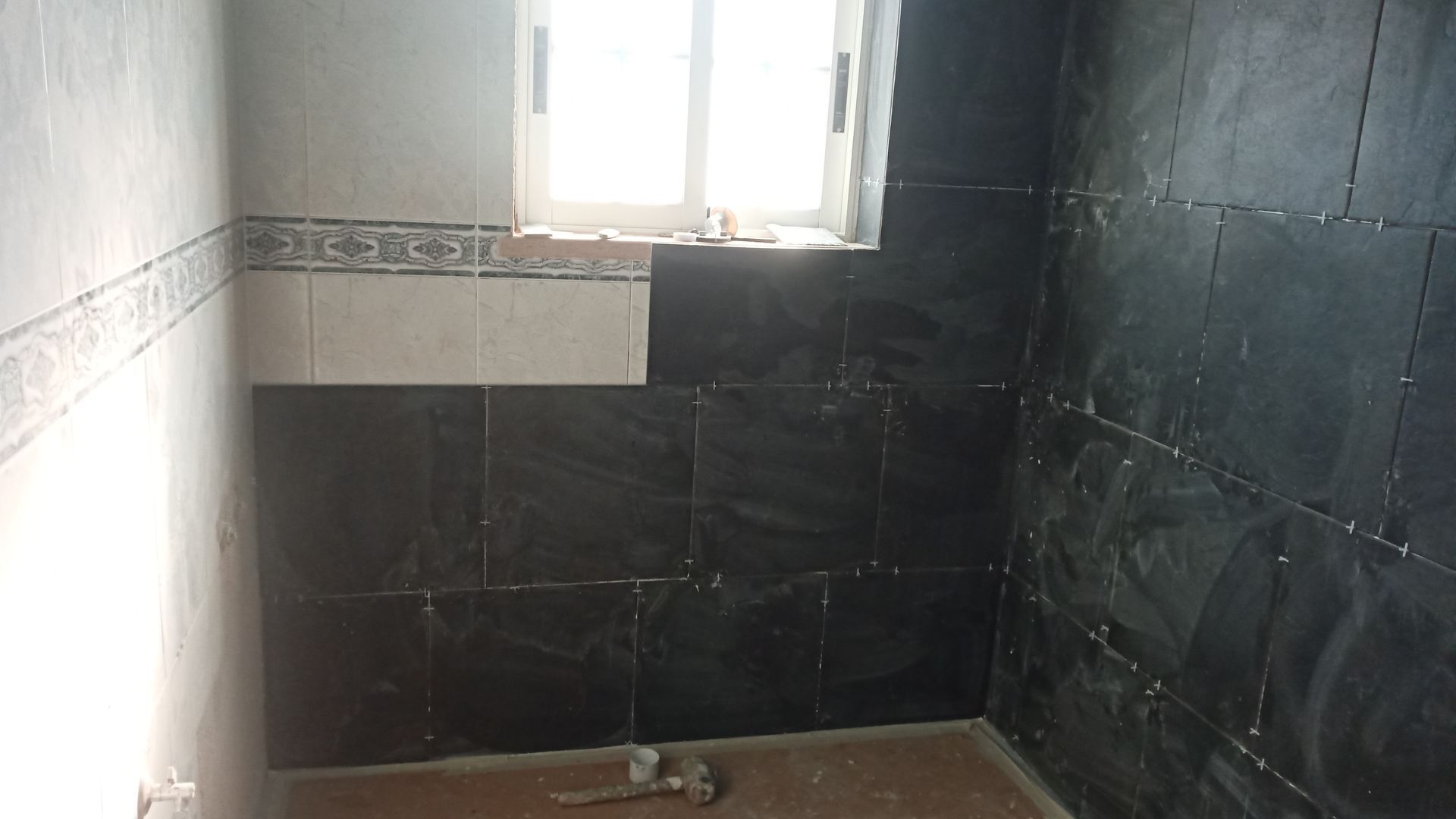 Banheiro com azulejos cinza-escuros nas paredes. Uma pequena janela é visível.