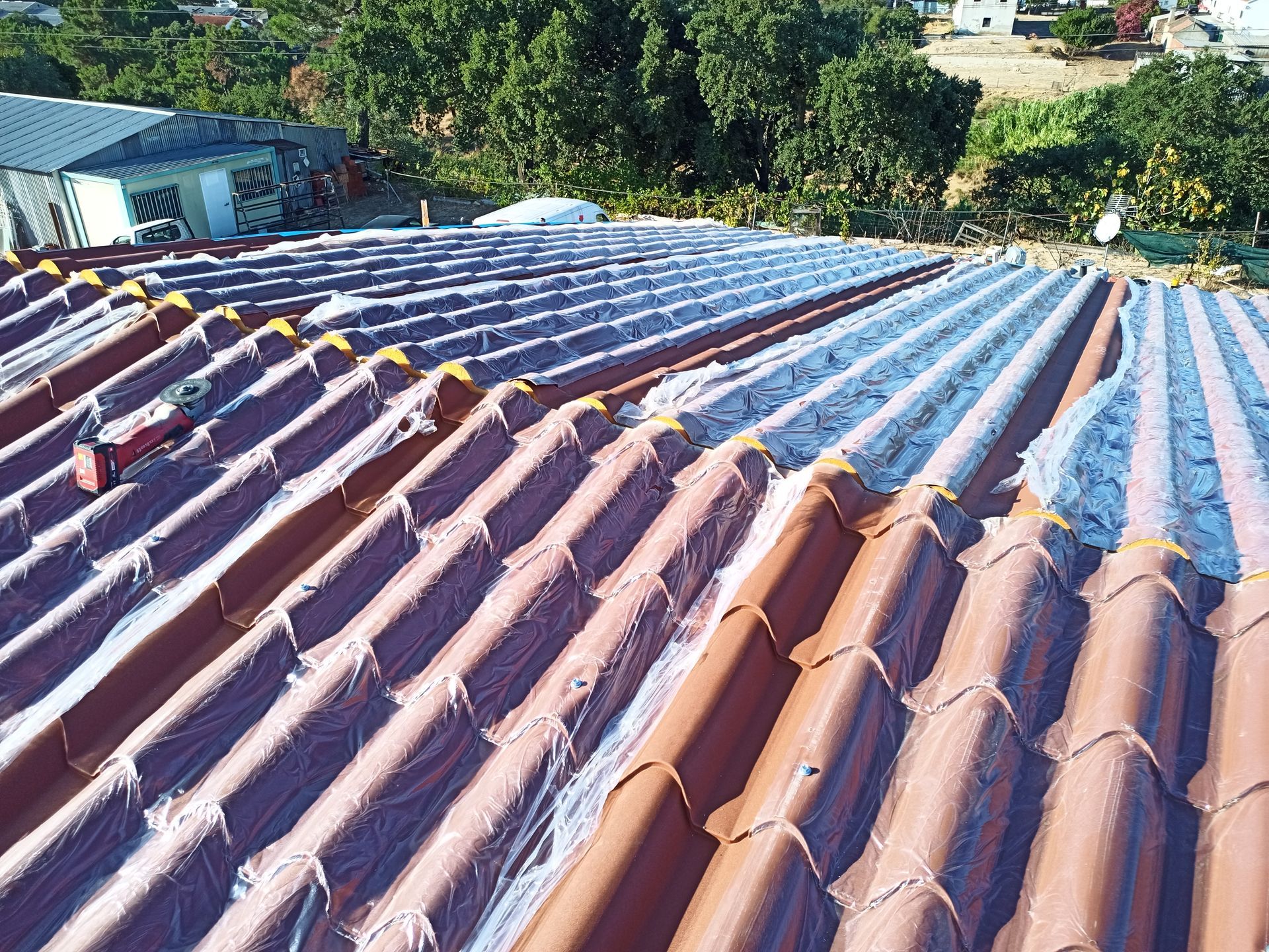Telhado de telhas de terracota parcialmente coberto com lona protetora branca.