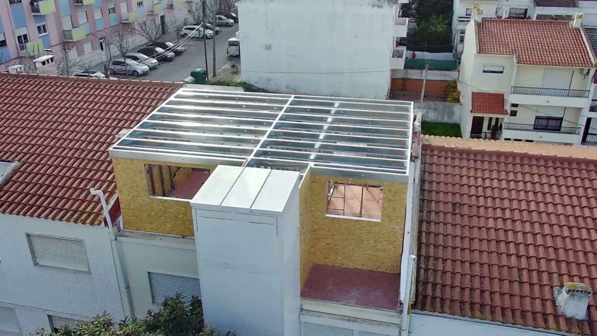 Estrutura de madeira em construção, cobertura com painéis de telha ondulada, edifícios circundantes, ambiente urbano.