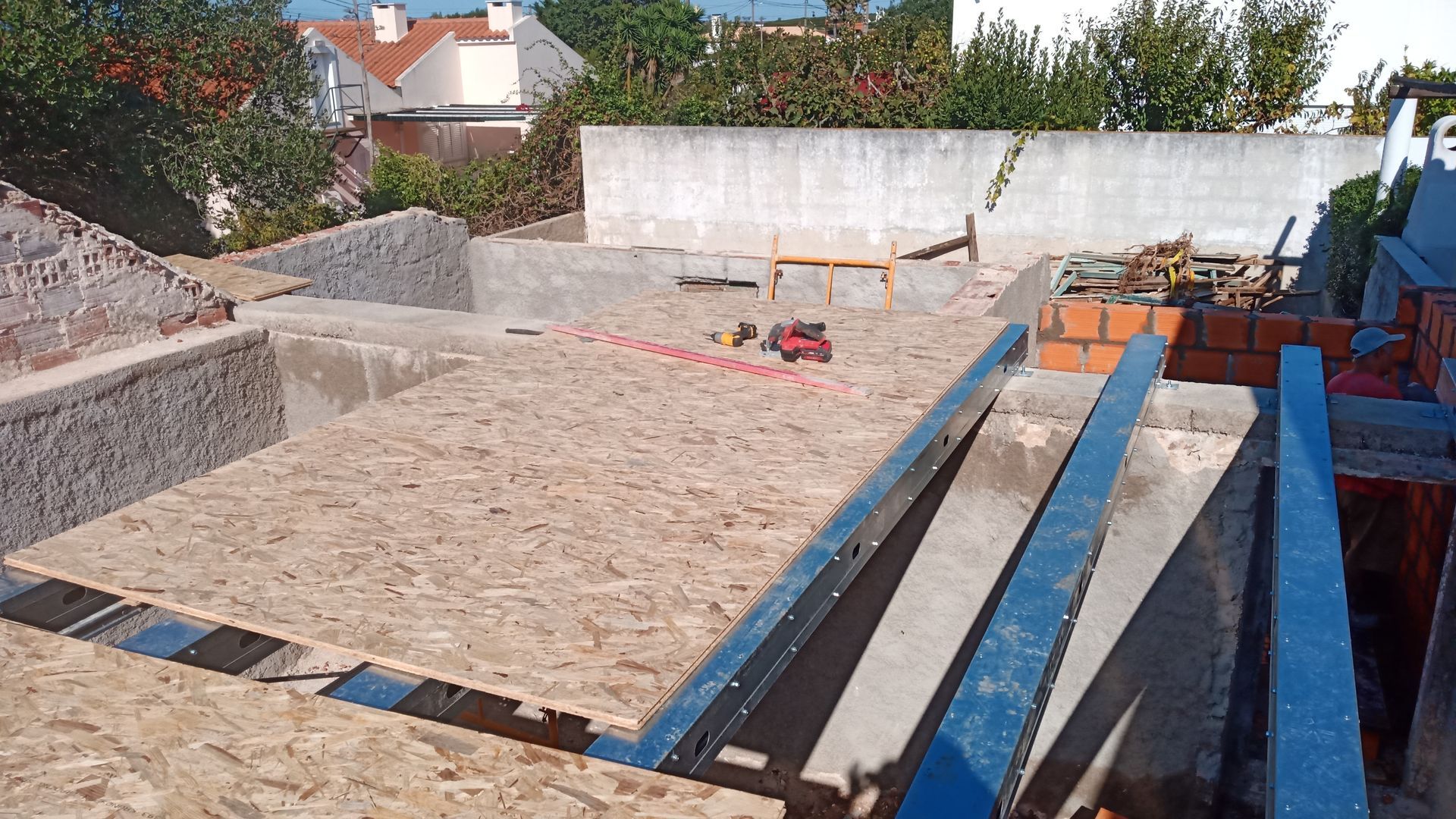 Canteiro de obras: placas de OSB assentadas sobre suportes metálicos, alvenaria, estrutura de cimento. Ao ar livre, com luz natural.