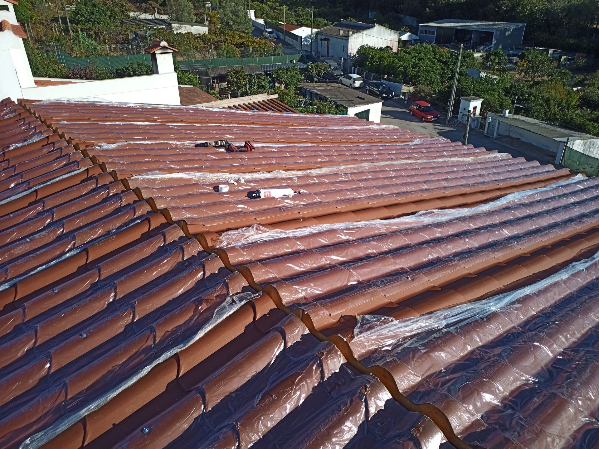 Telhado de telha marrom parcialmente coberto com plástico transparente, ao ar livre.