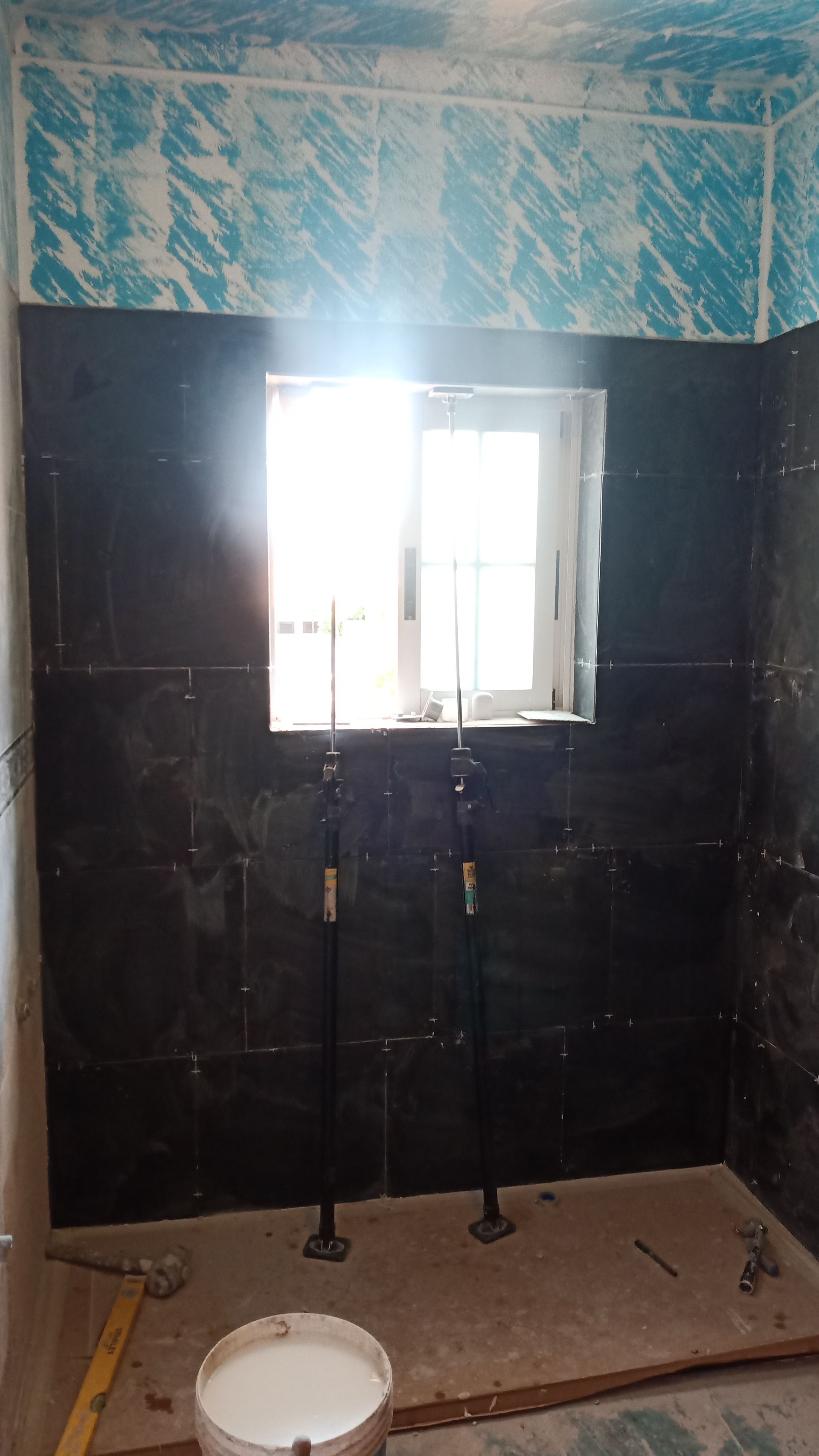 Banheiro em reforma com azulejos pretos, janela e encanamento aparente.