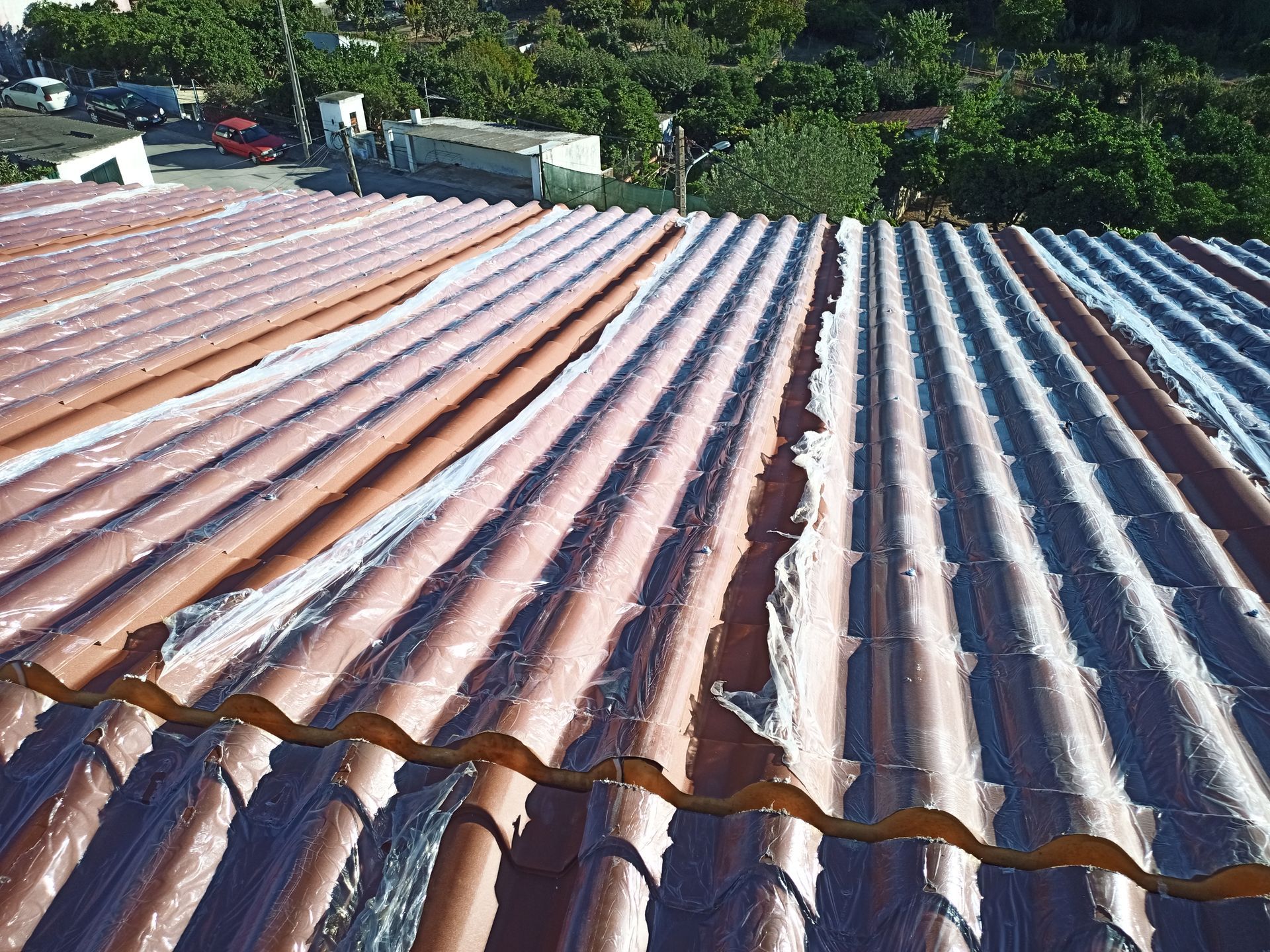 Telhado de zinco danificado com revestimento descascando, com vista para árvores verdes e edifícios.