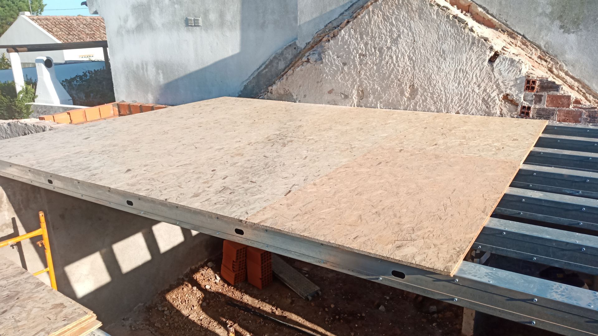 Placa de concreto apoiada em vigas metálicas, canteiro de obras com parede de tijolos e acabamento inacabado.