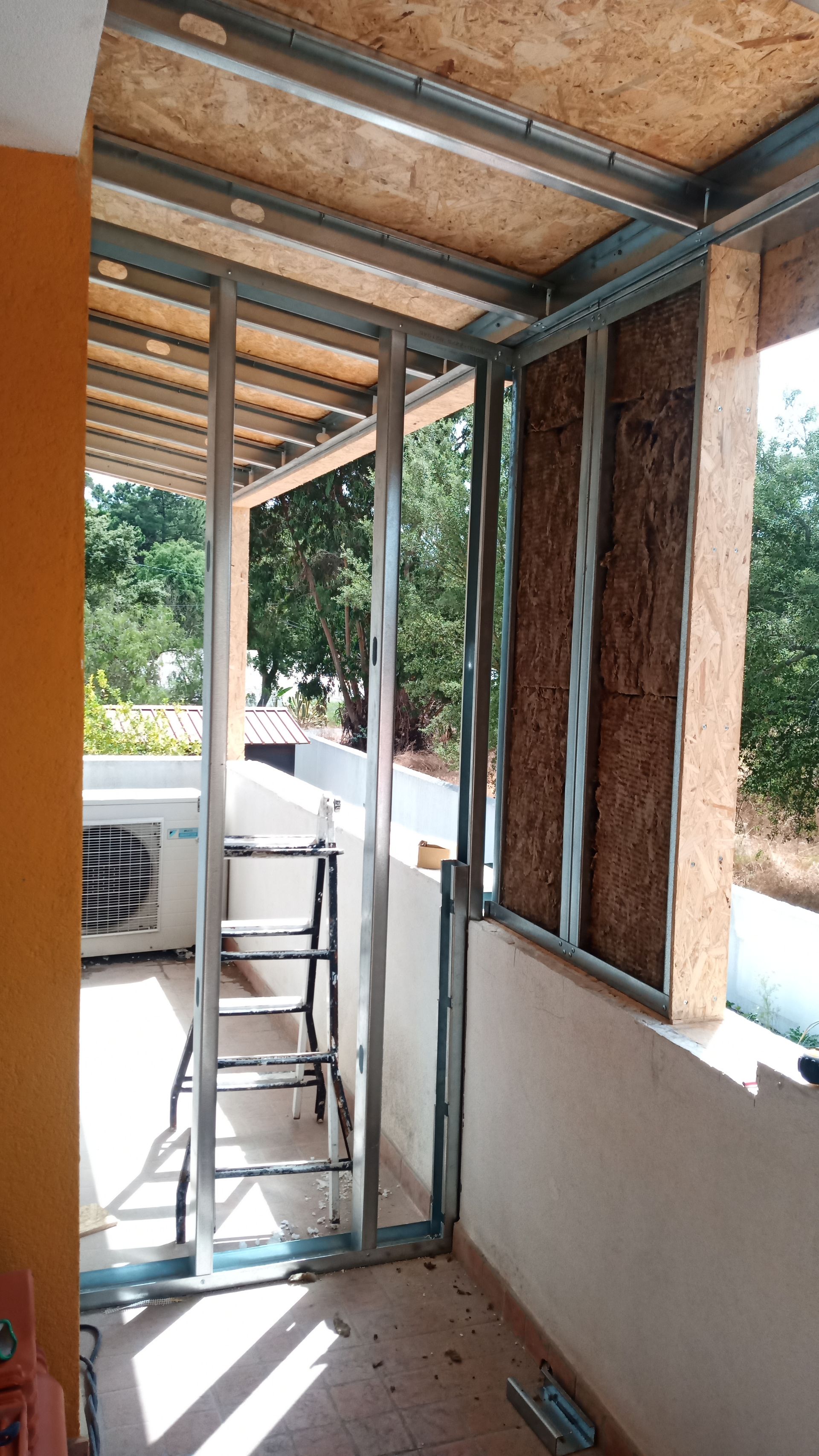 Estrutura metálica para parede externa e teto, com painéis de madeira. Há uma pequena escada no local.