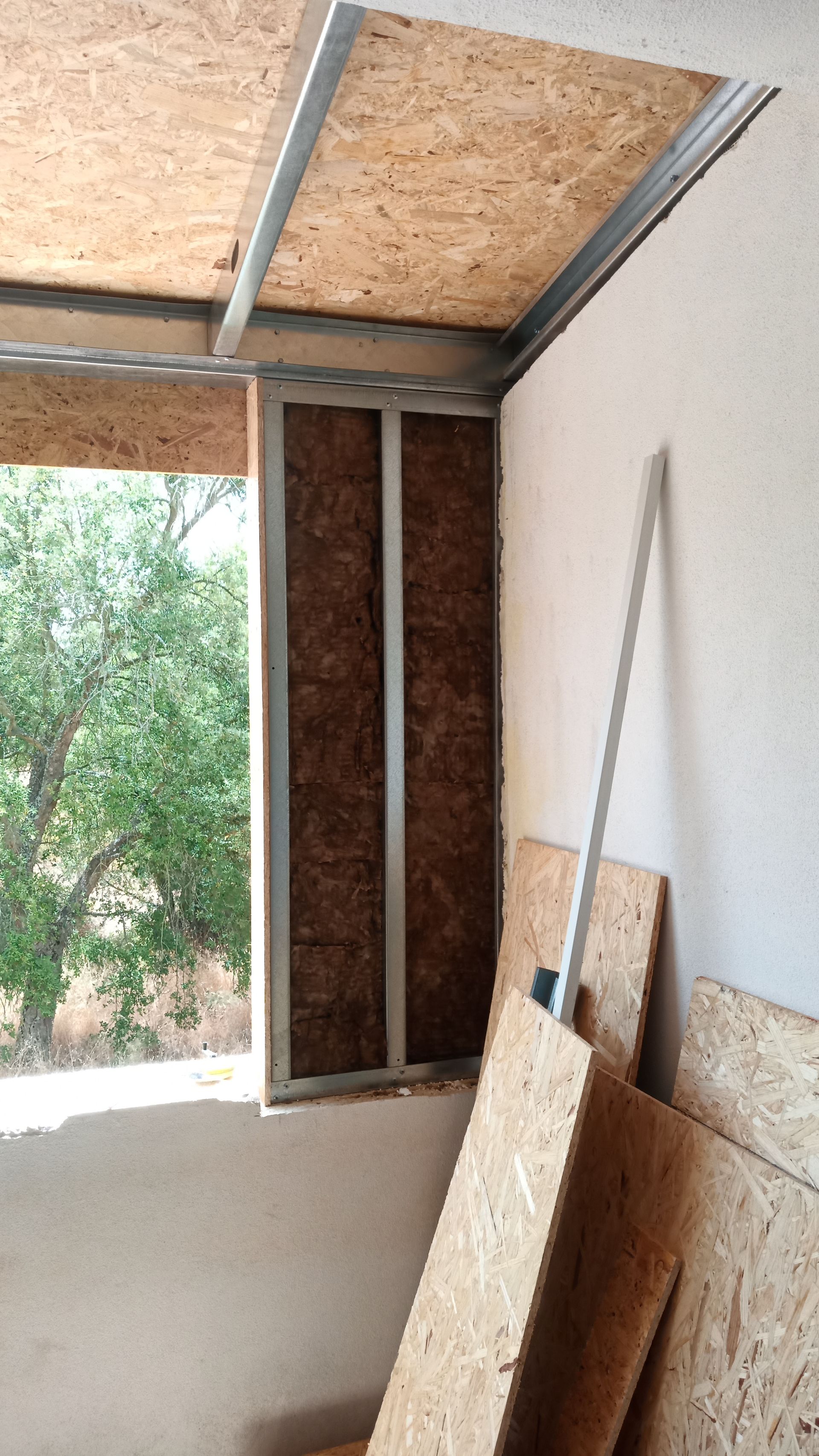 Placas de OSB e estrutura metálica ao redor de uma janela, mostrando a construção em andamento.