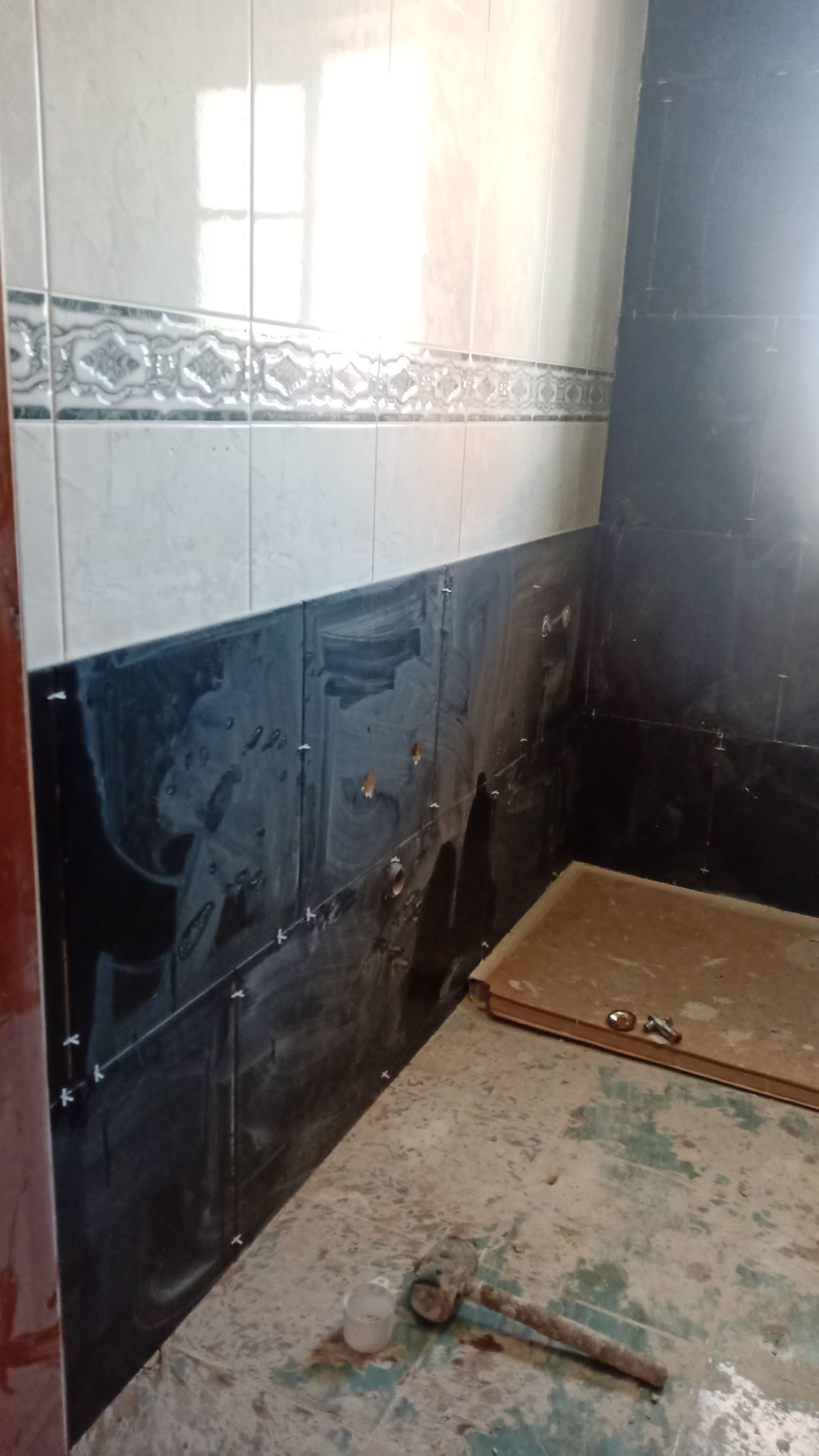 Banheiro em construção; azulejos pretos e brancos nas paredes, piso inacabado.