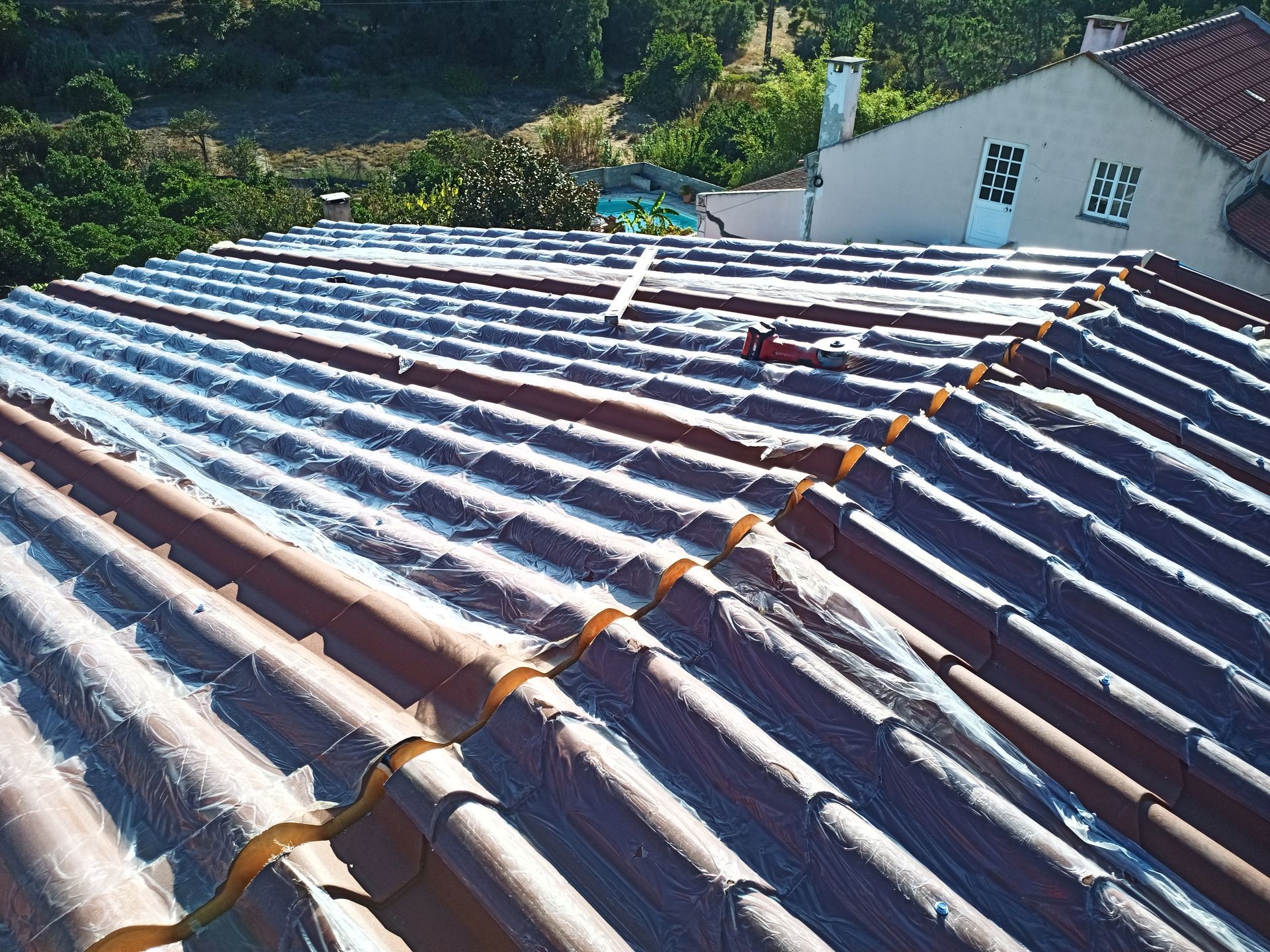 Telhado de telhas vermelhas com uma substância branca. Prédios e árvores ao fundo.