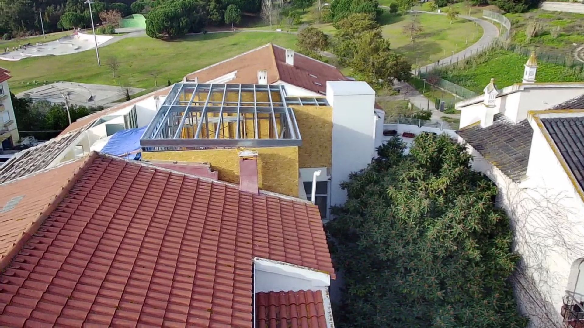Telhados de edifícios, um deles com estrutura metálica exposta, com um parque ao fundo.