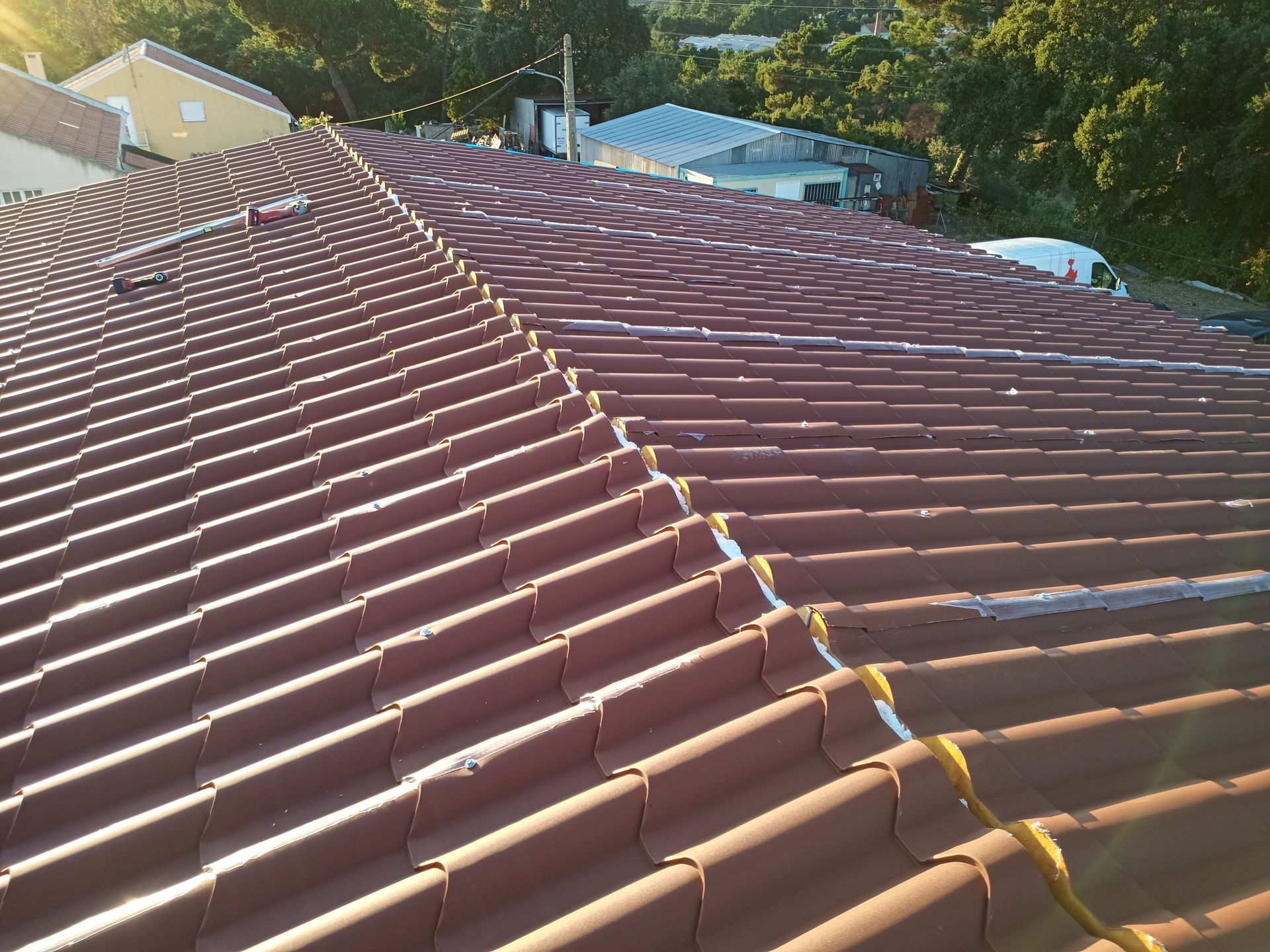 Telhado de telha vermelha com cumeeiras, visto de cima em um dia ensolarado.