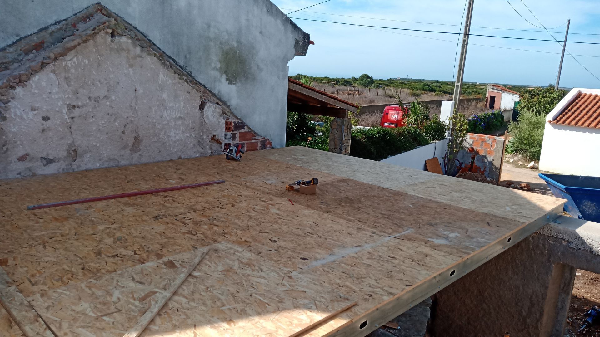 Telhado em construção com um grande painel de madeira, adjacente a um edifício deteriorado.