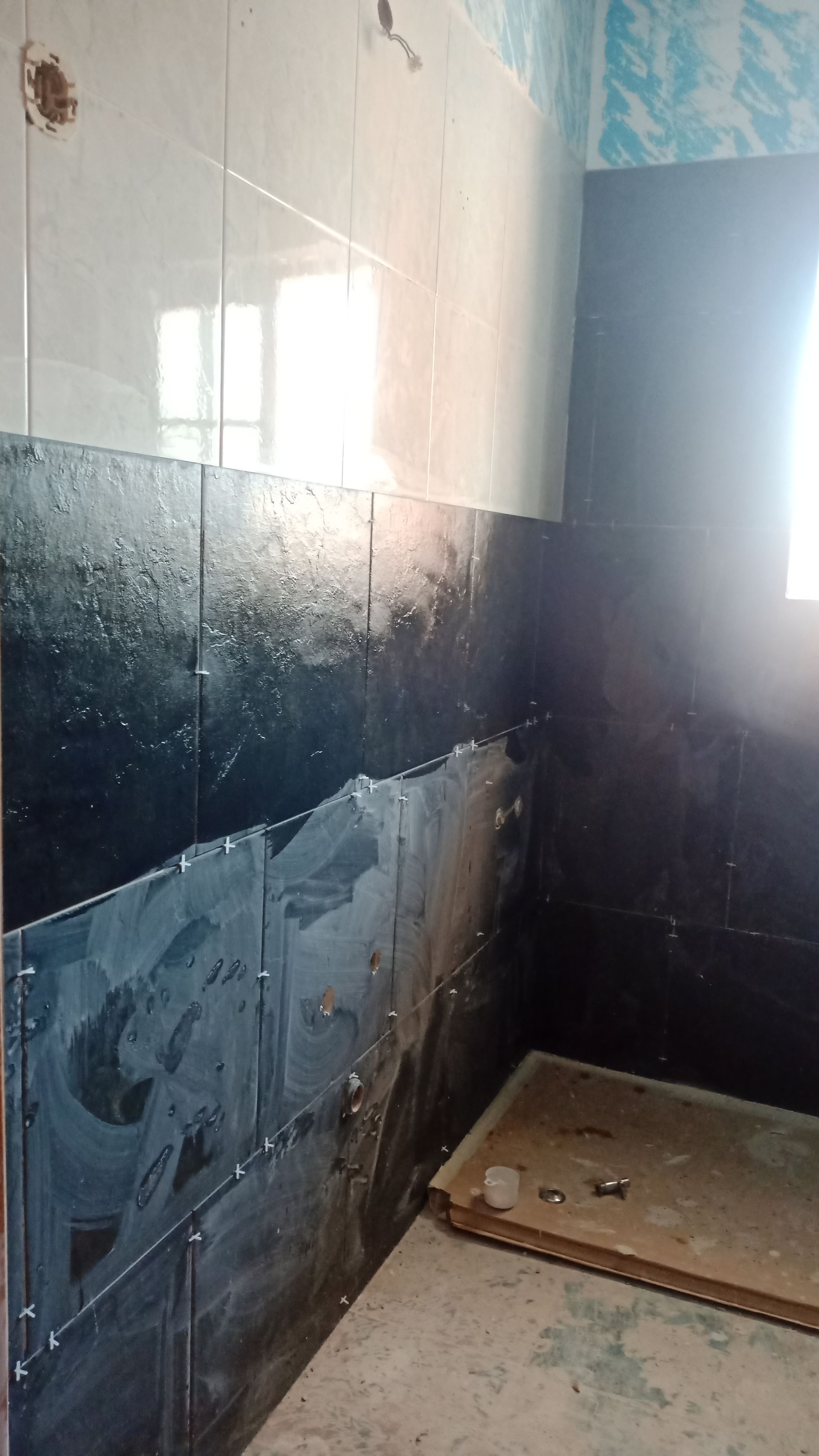 Banheiro em construção com azulejos pretos e brancos nas paredes e compensado no piso.