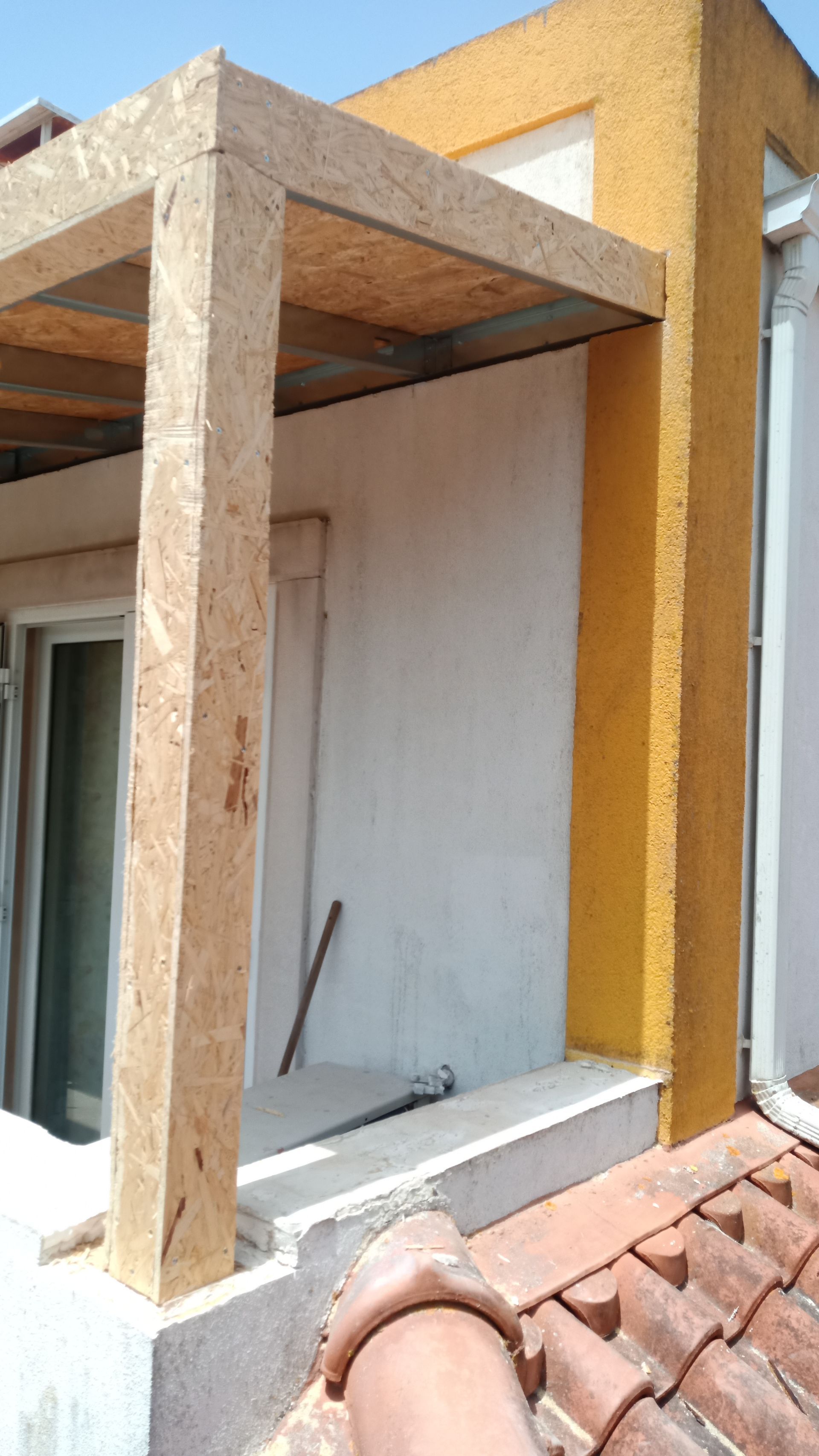 Viga de madeira sustentando o telhado de uma varanda, com um trecho de parede em amarelo.