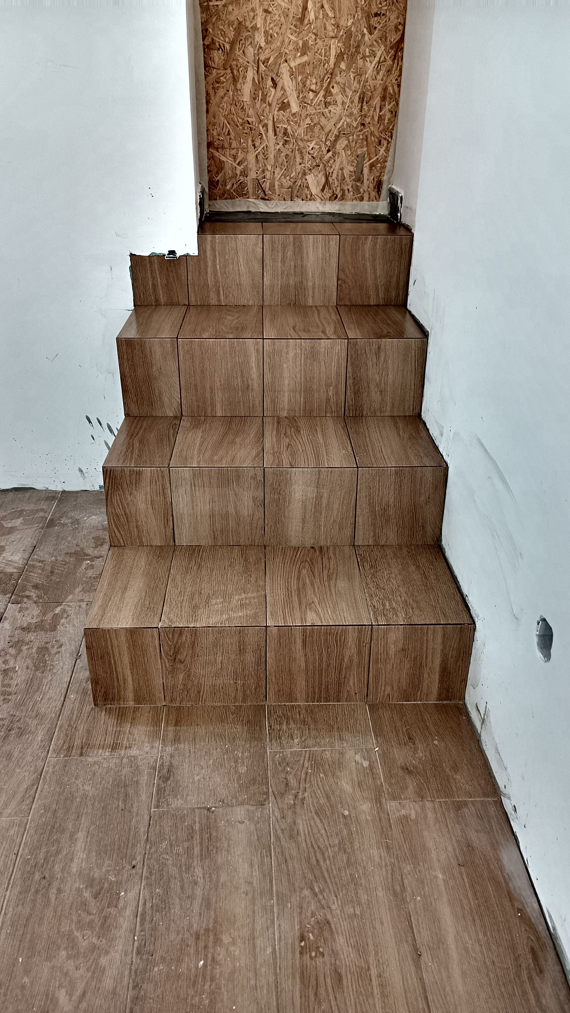 Escada com azulejos marrons que leva ao andar superior, com piso e paredes brancas combinando.