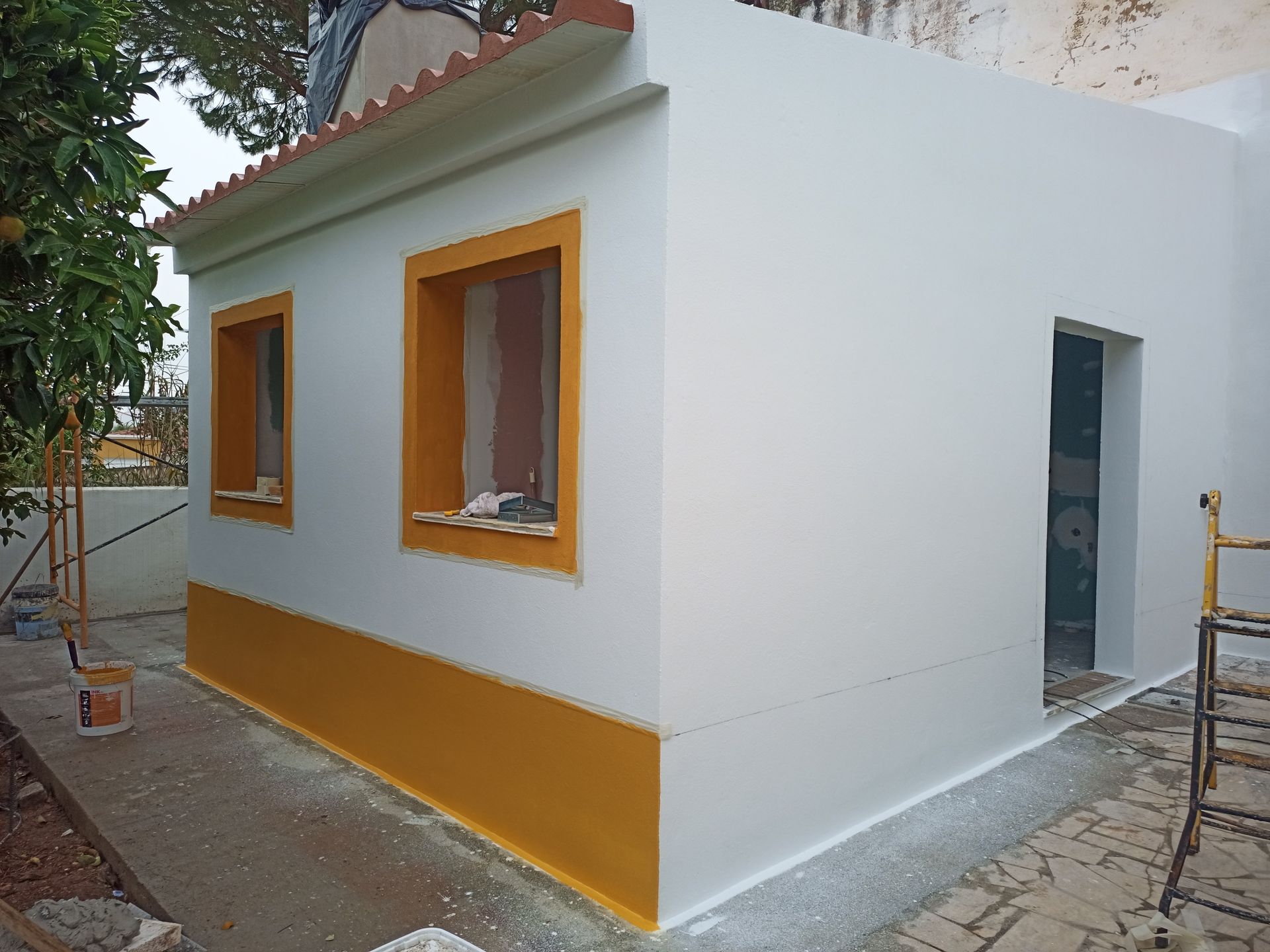 Prédio branco com detalhes, janelas e beiral do telhado em amarelo. Porta de entrada visível.