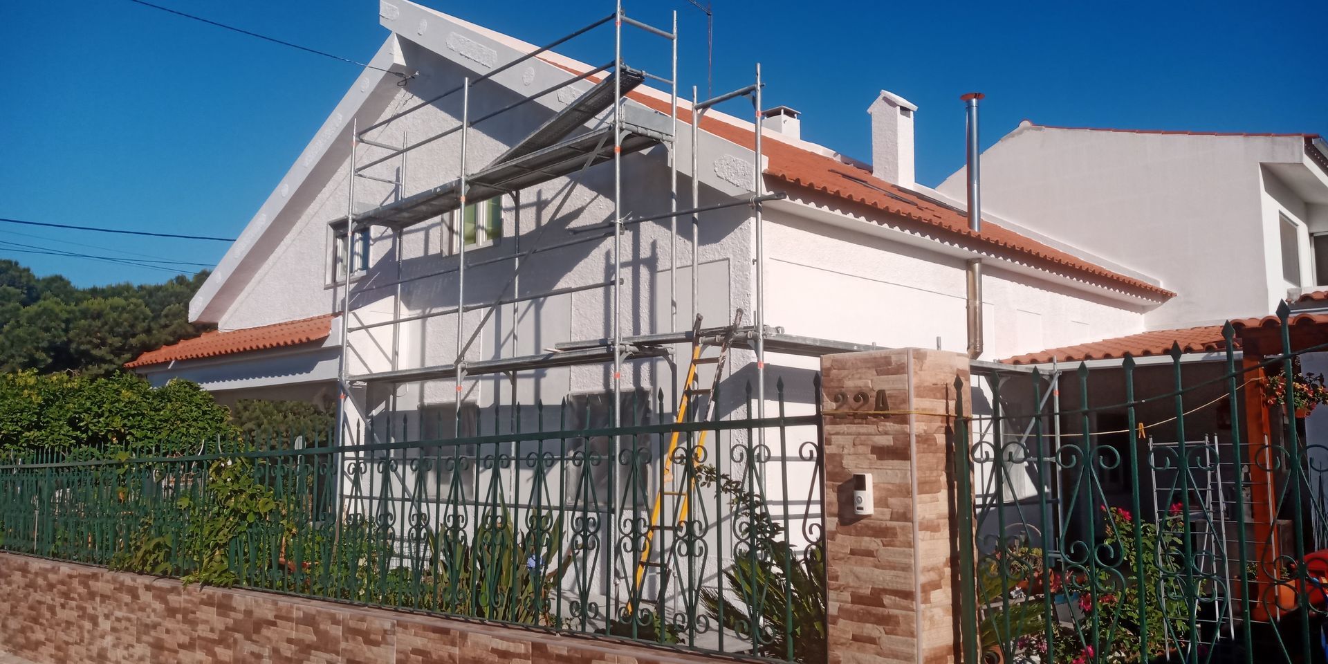 Uma casa branca com telhado de telhas vermelhas está passando por reformas com andaimes.