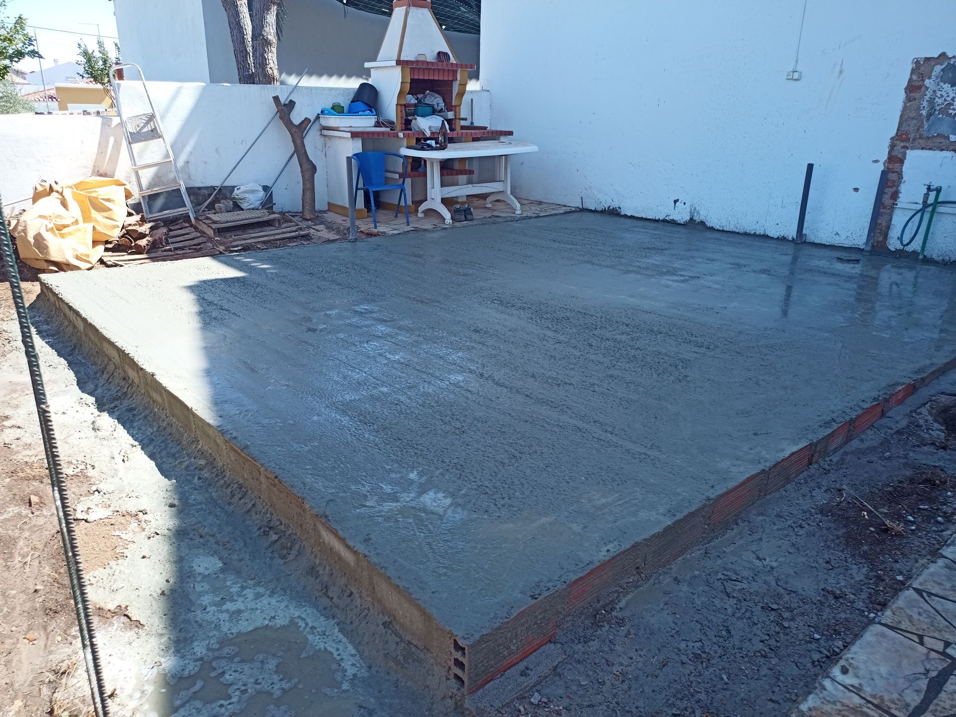 Pátio de concreto recém-construído, delimitado por madeira, com ferramentas e materiais por perto.