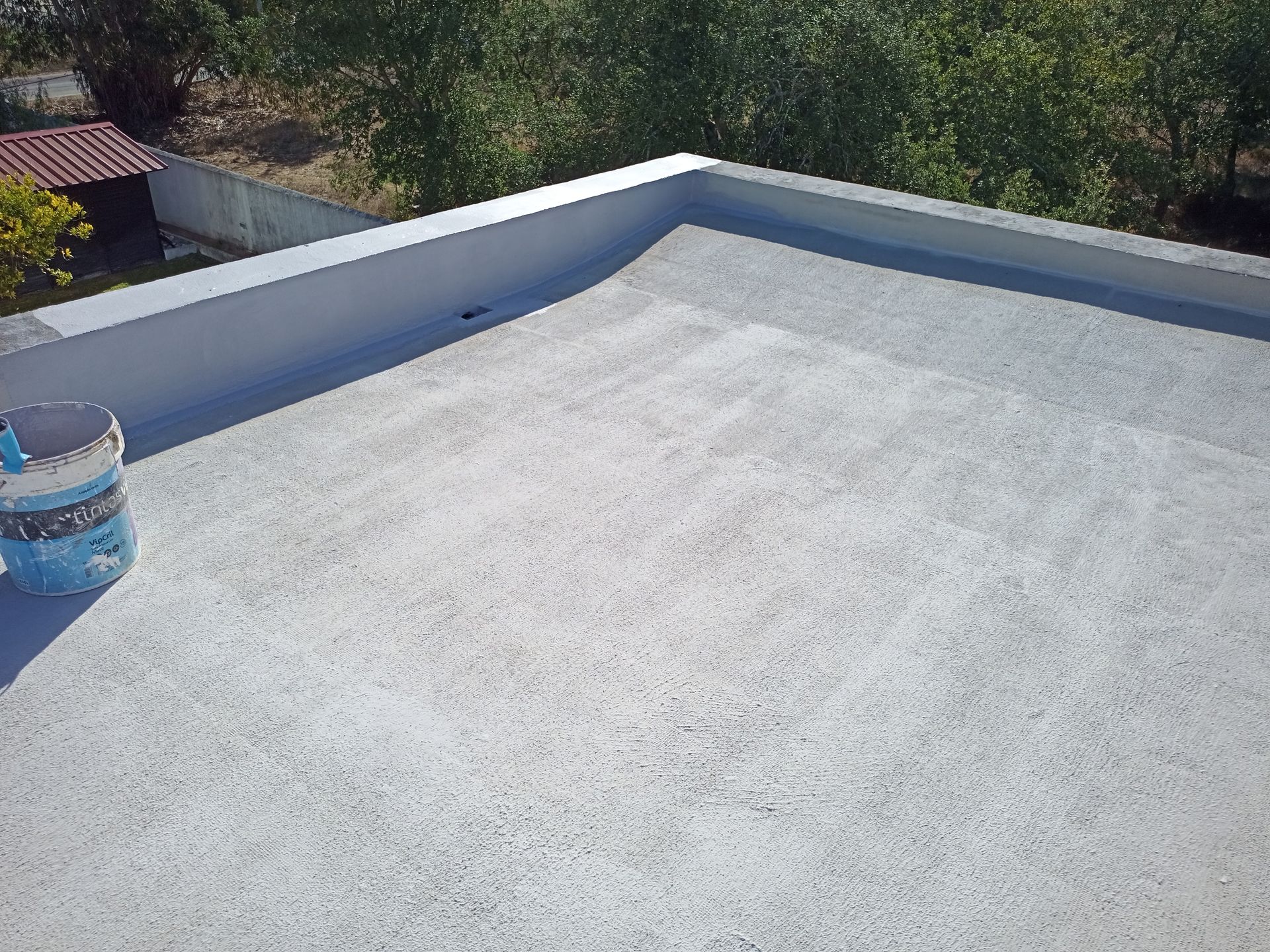 Telhado plano com revestimento cinza claro e um balde de tinta.