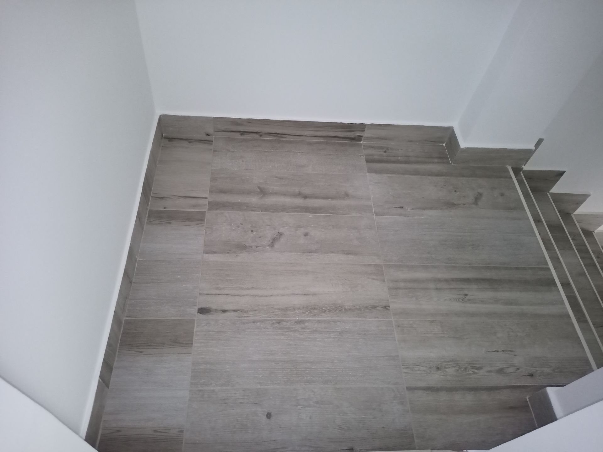 Pisos e paredes revestidos com azulejos cinza encontram paredes e escadas brancas.