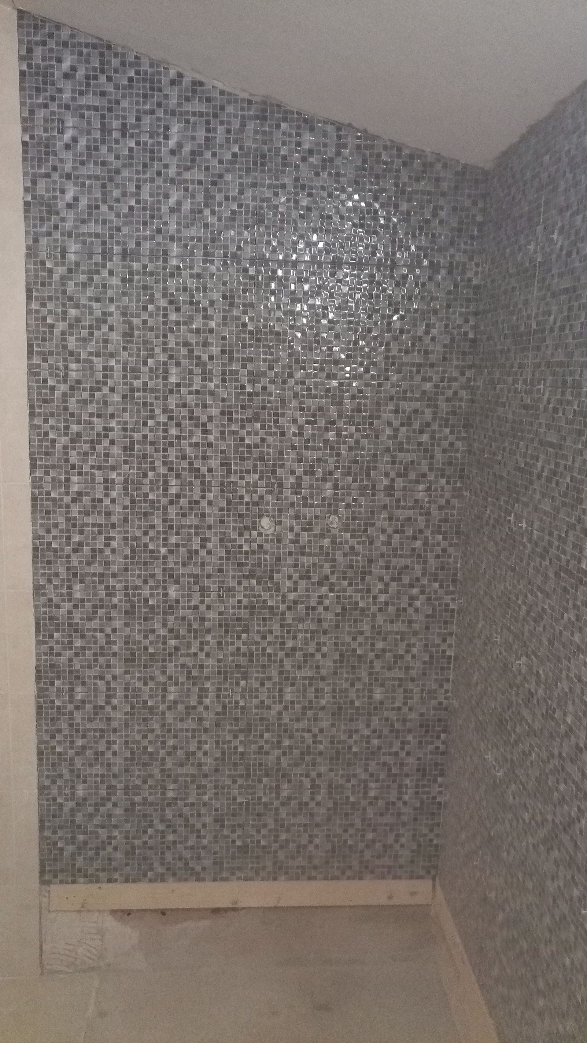 Paredes do chuveiro revestidas com azulejos de mosaico cinza.