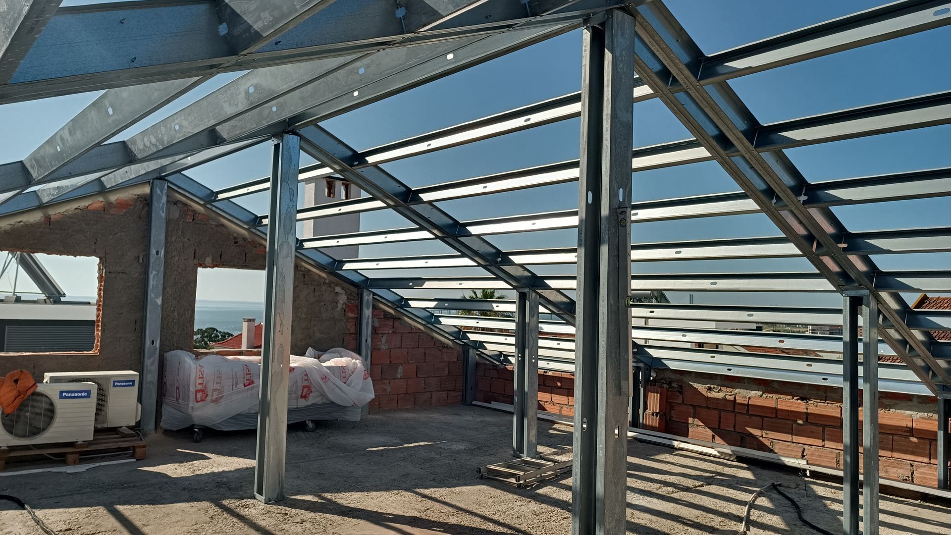 Telhado com estrutura metálica em construção sobre paredes de tijolo.